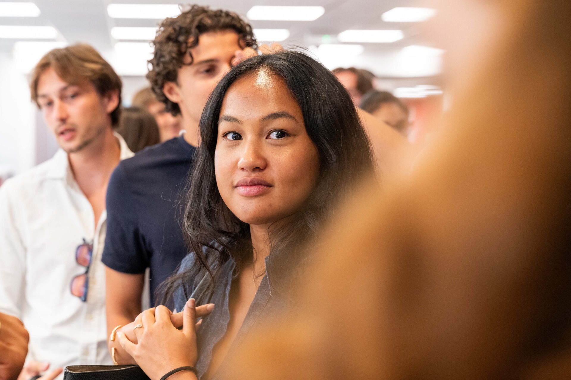 A young woman looking at the camera, with a blurred crowd in the background and a brown foreground blur.
