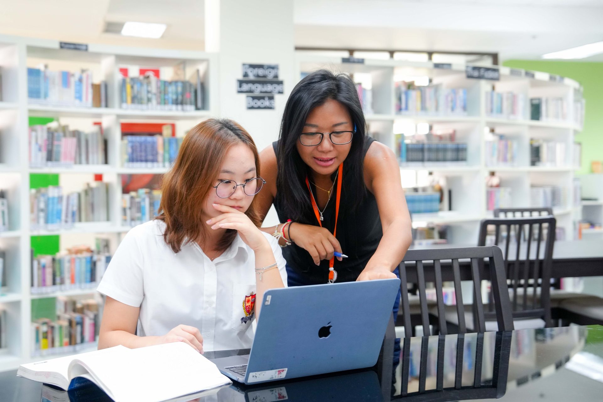 Student and teacher collaborate on a laptop in a bright library.