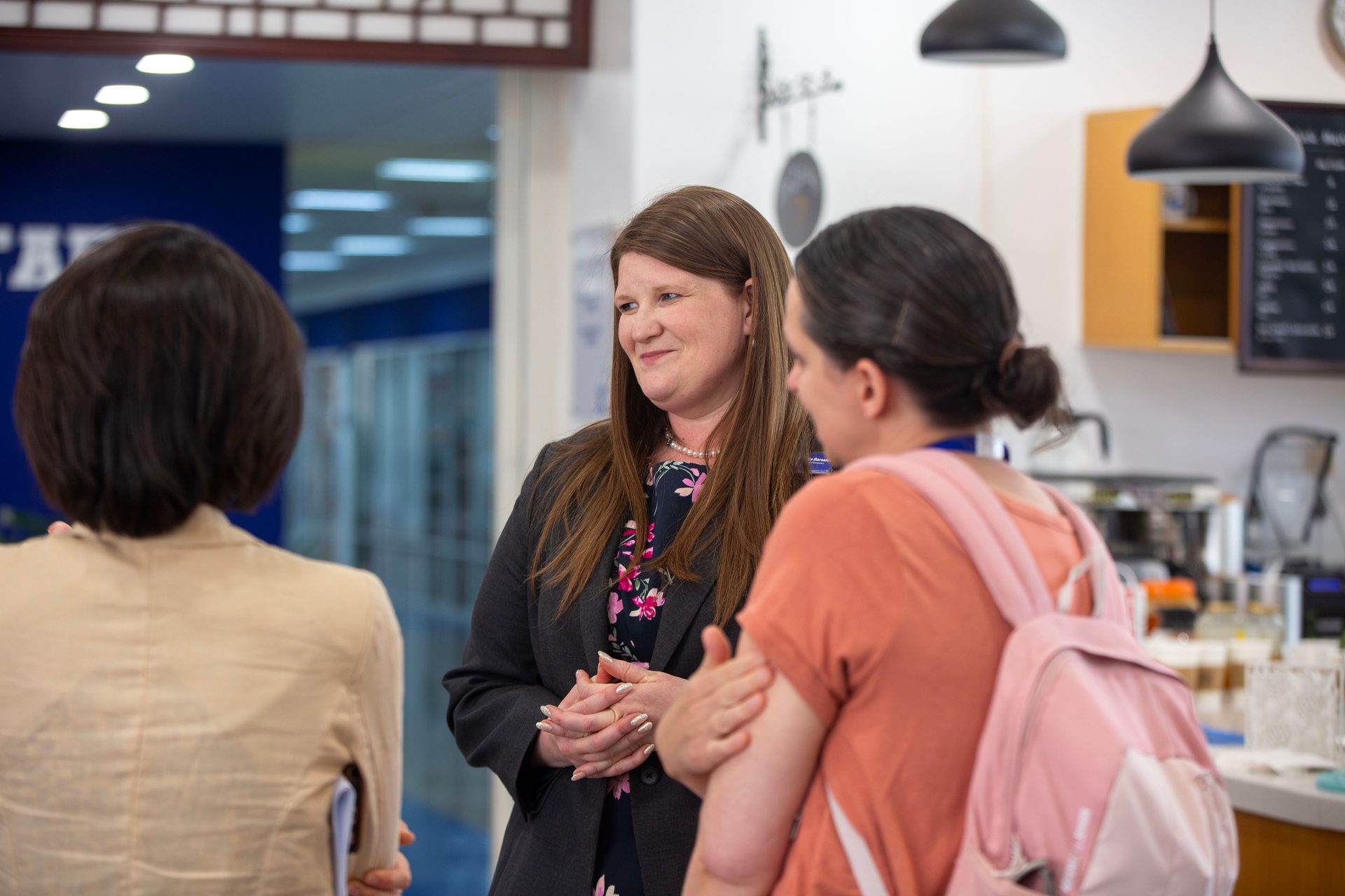 Smiling woman in suit conversing with two other women indoors.