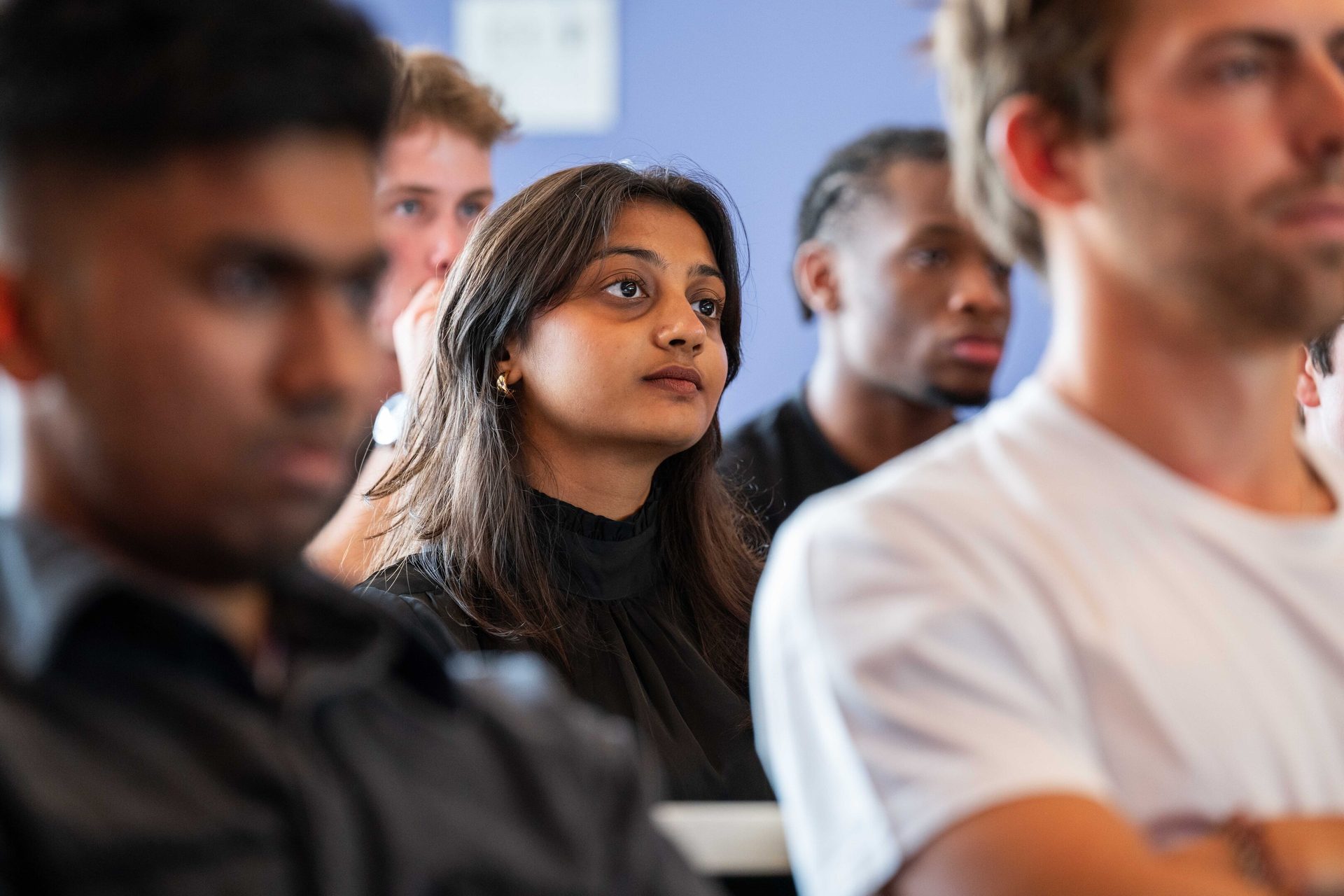 Young woman intently listening or watching in a diverse group.