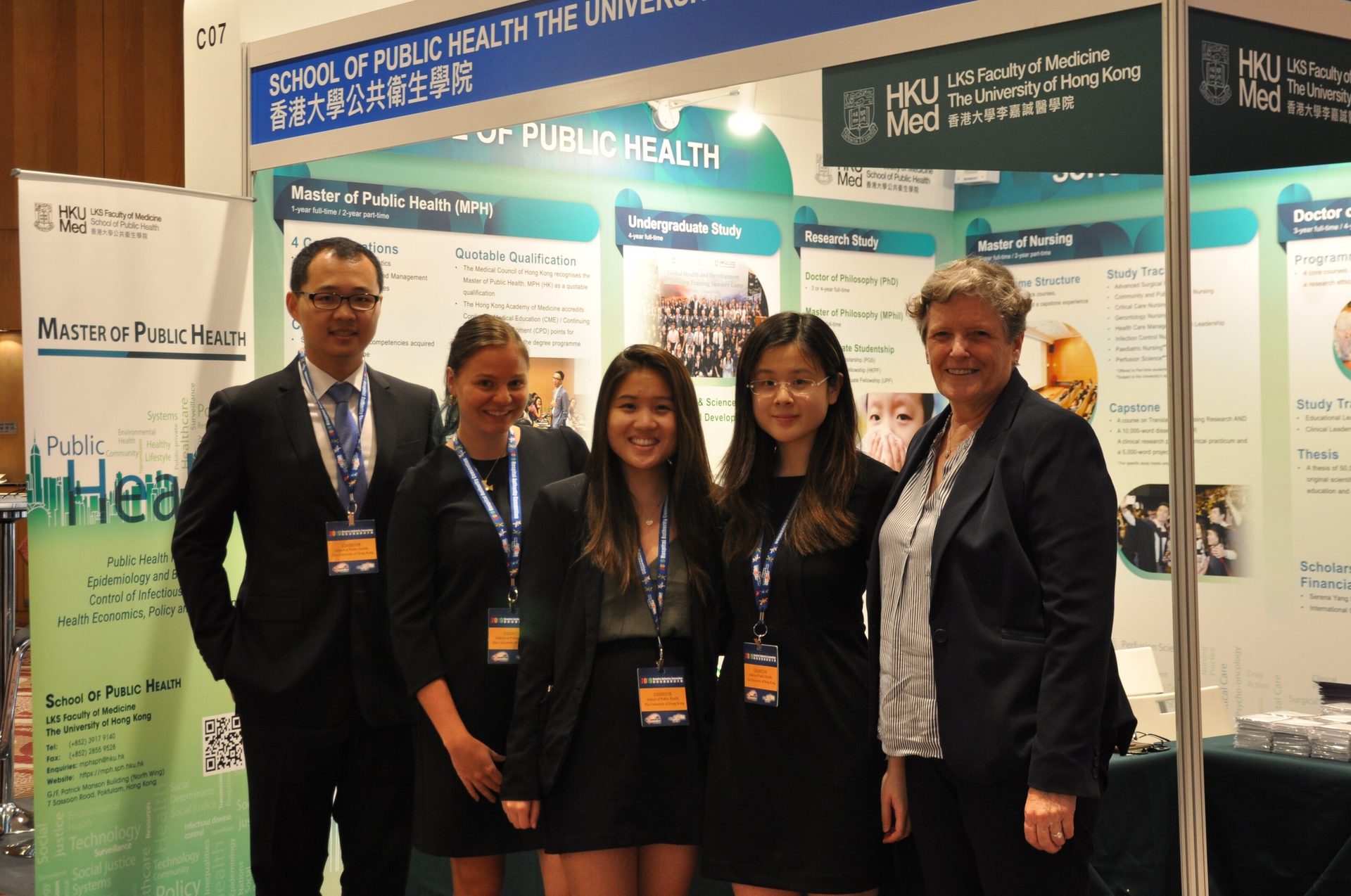 Five people (one man, four women) smiling at HKU School of Public Health informational booths.