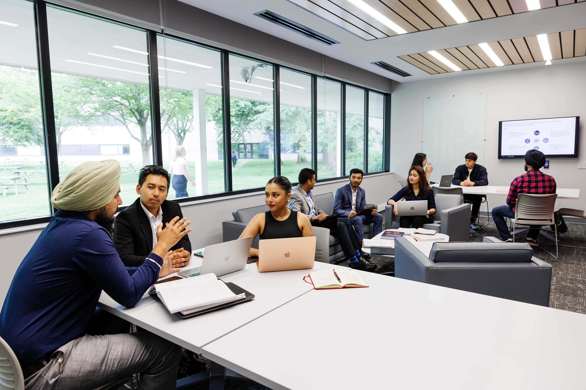 Diverse group meeting in a bright, modern office with laptops and large windows.