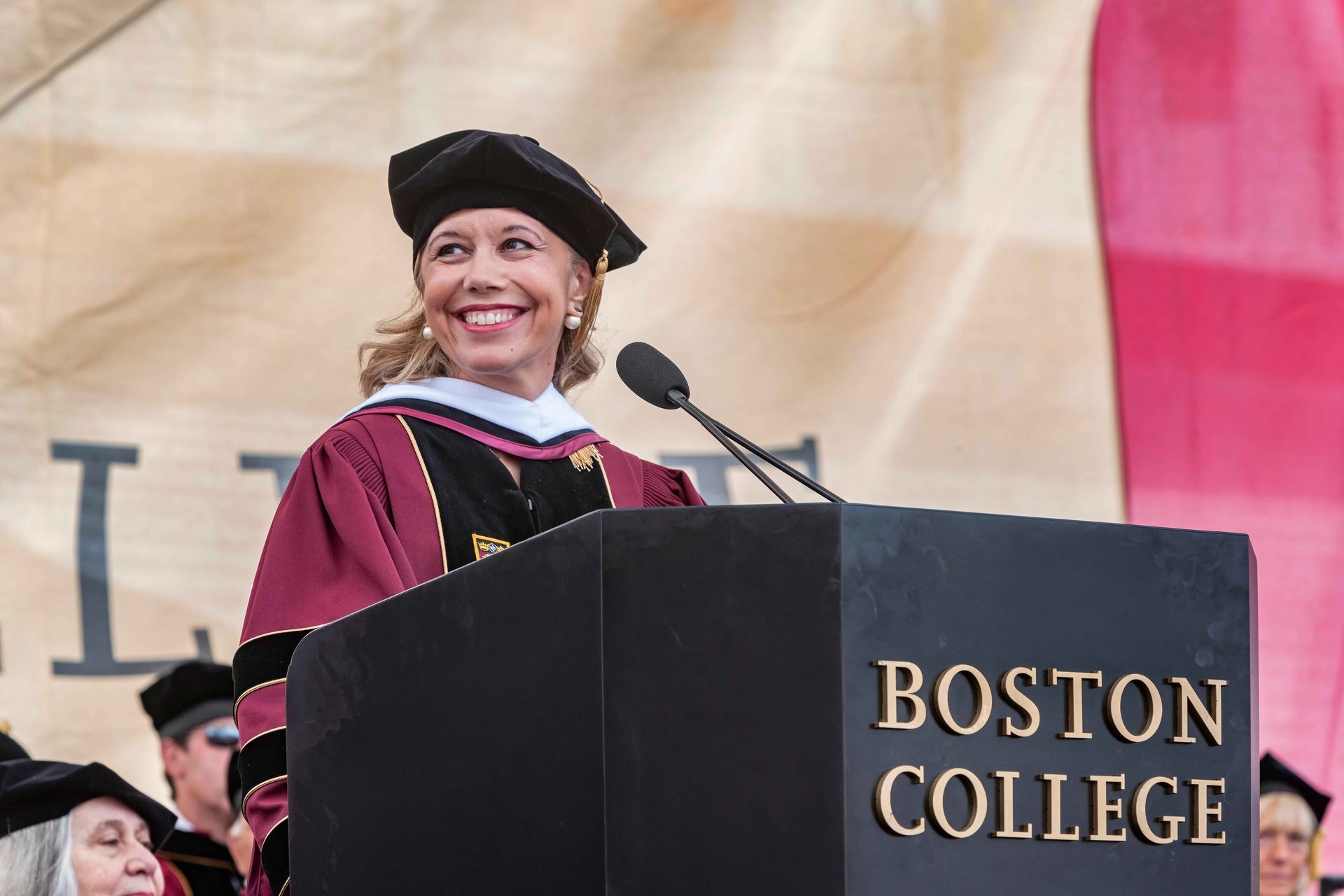 Public address system, Academic dress, Microphone, Smile, Podium, Lectern, Scholar, Mortarboard, Gesture, Headgear