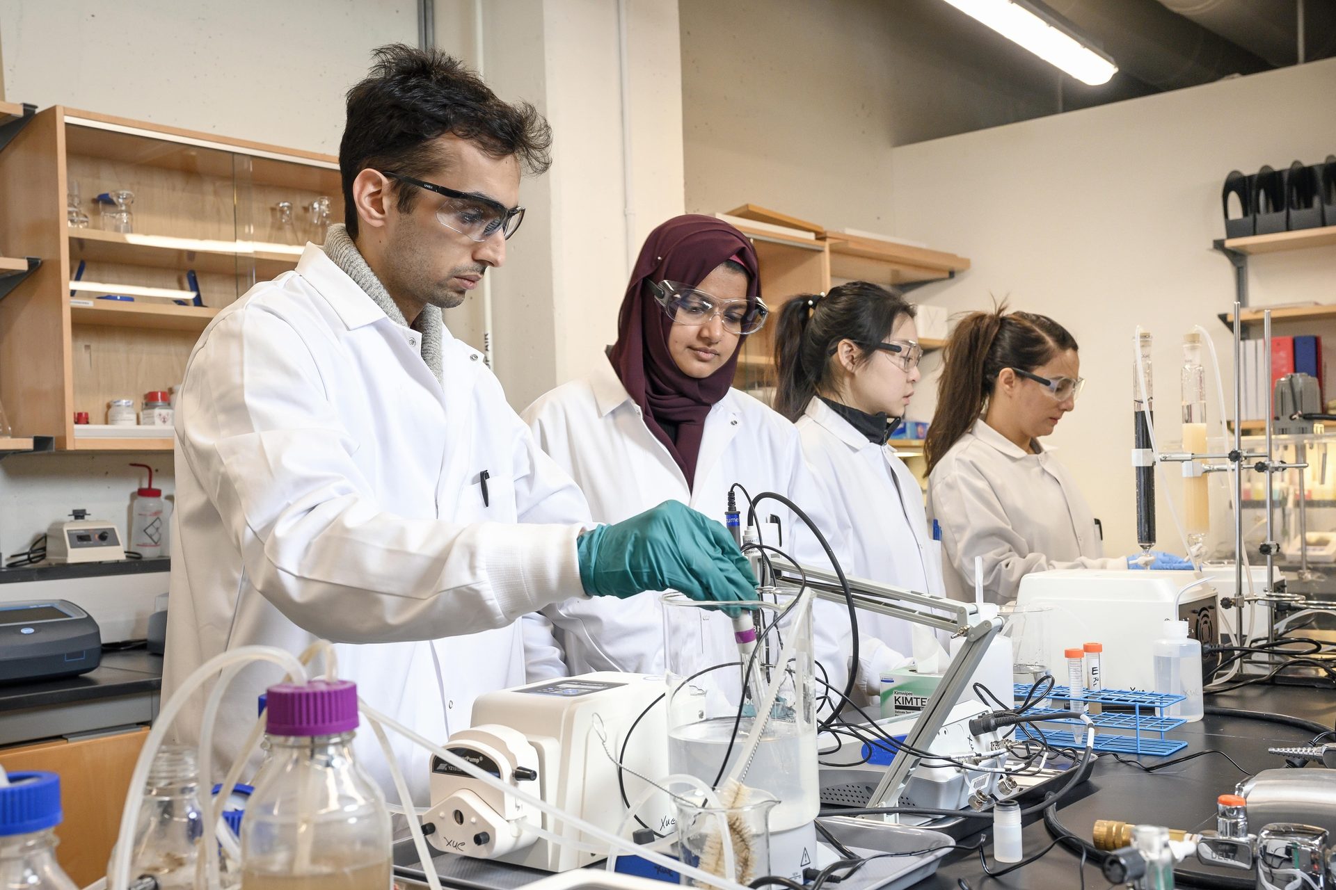 Researchers in lab coats and safety glasses working with scientific equipment in a lab.