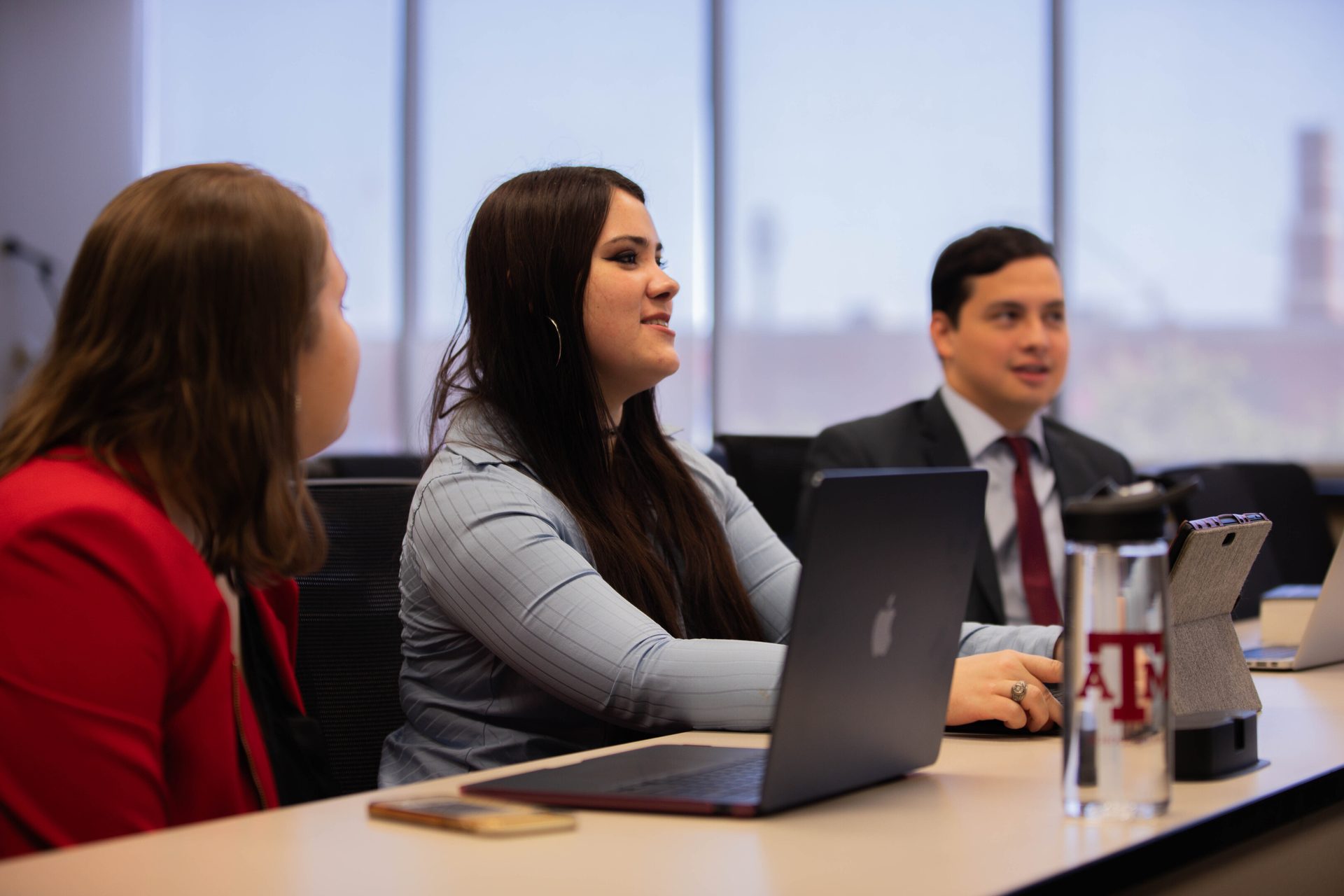 Three individuals, two women and one man, seated at a table with laptops, engaged in a discussion.