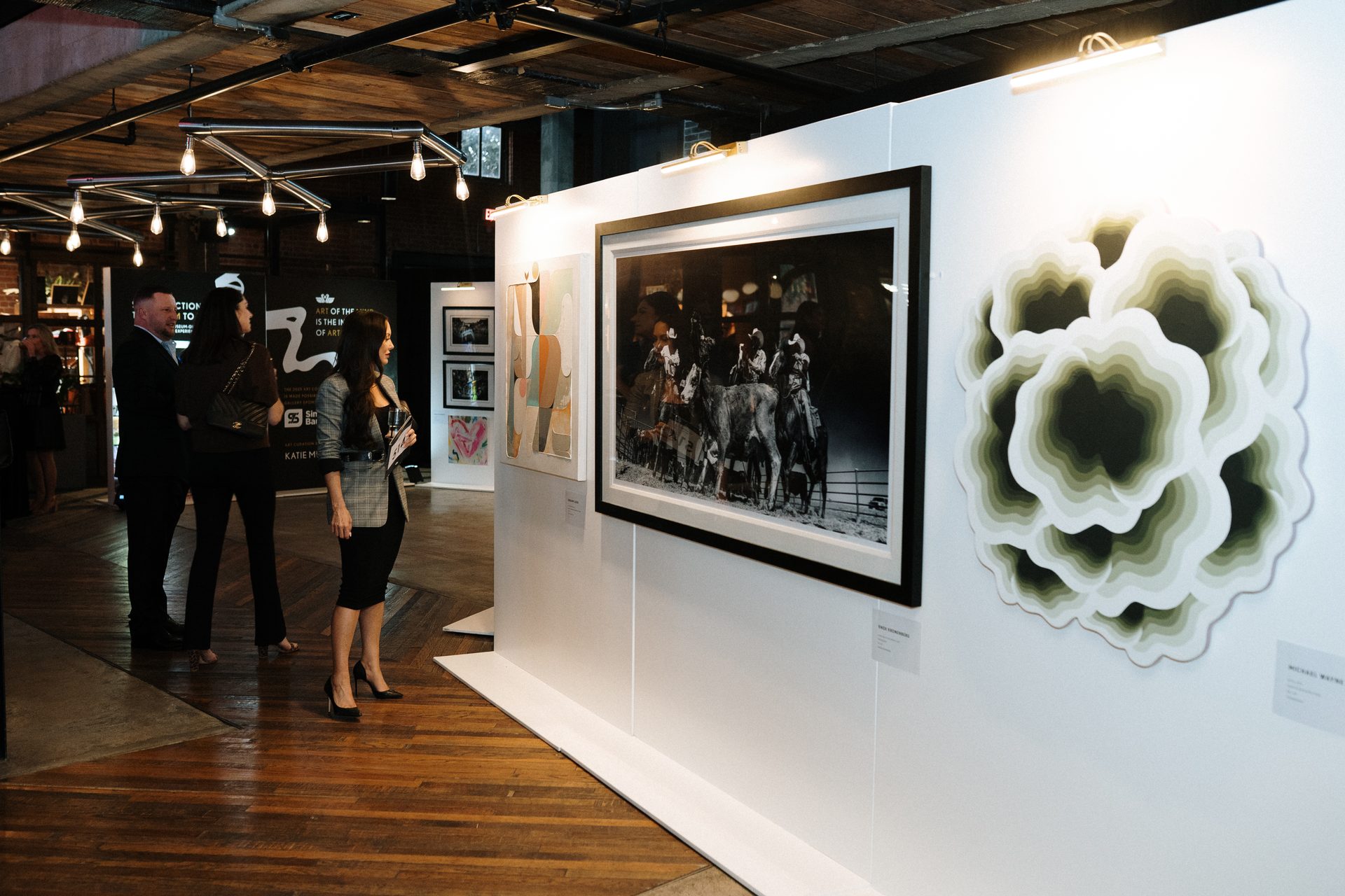 Visitors view a large black & white photo and a layered sculpture at an art exhibition.