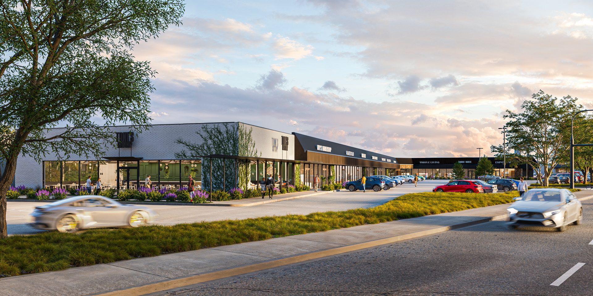 Modern retail complex with storefronts, cafes, parking, moving cars, and people at dusk.