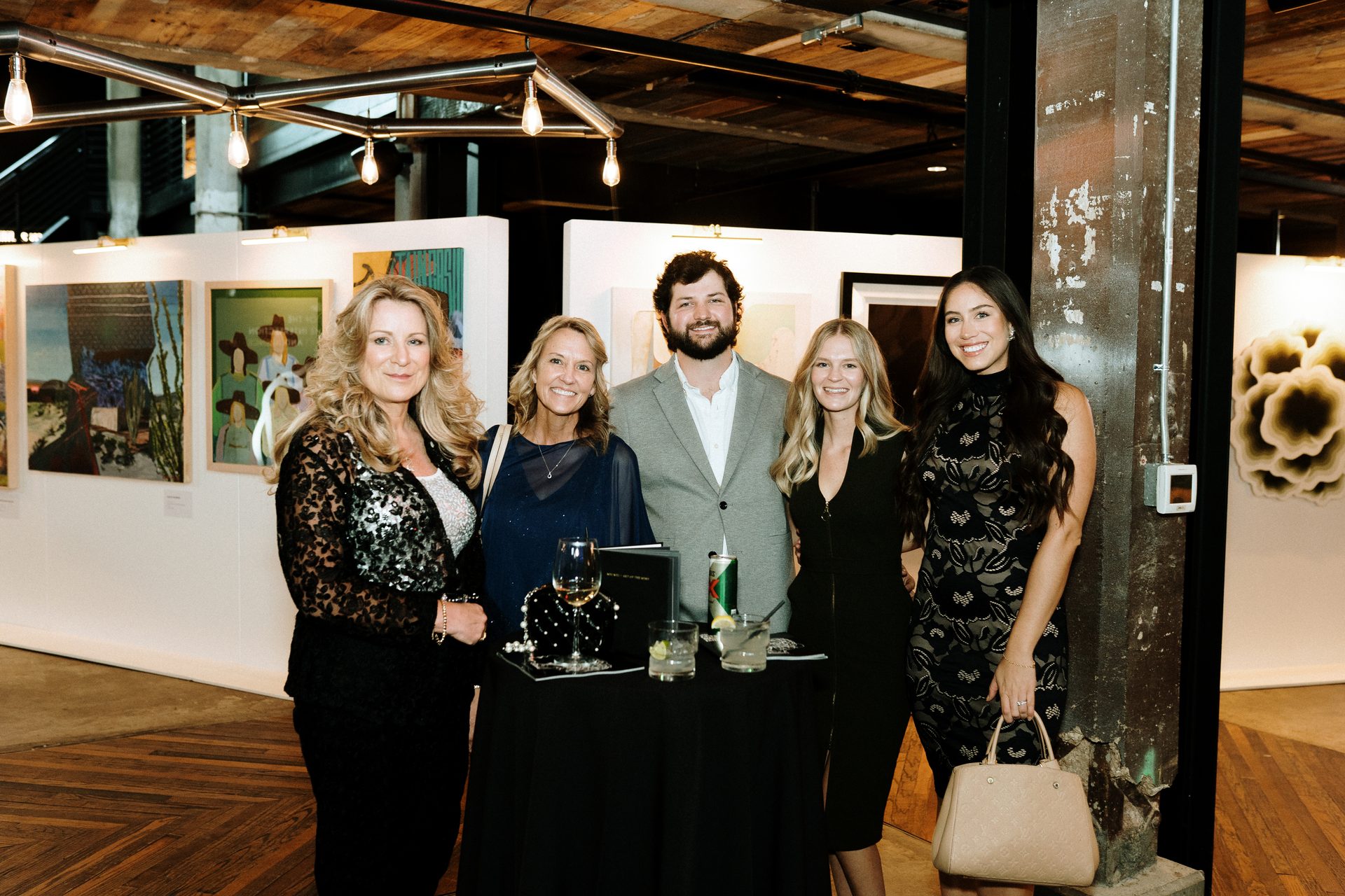 Four women and one man smiling at an art exhibition.