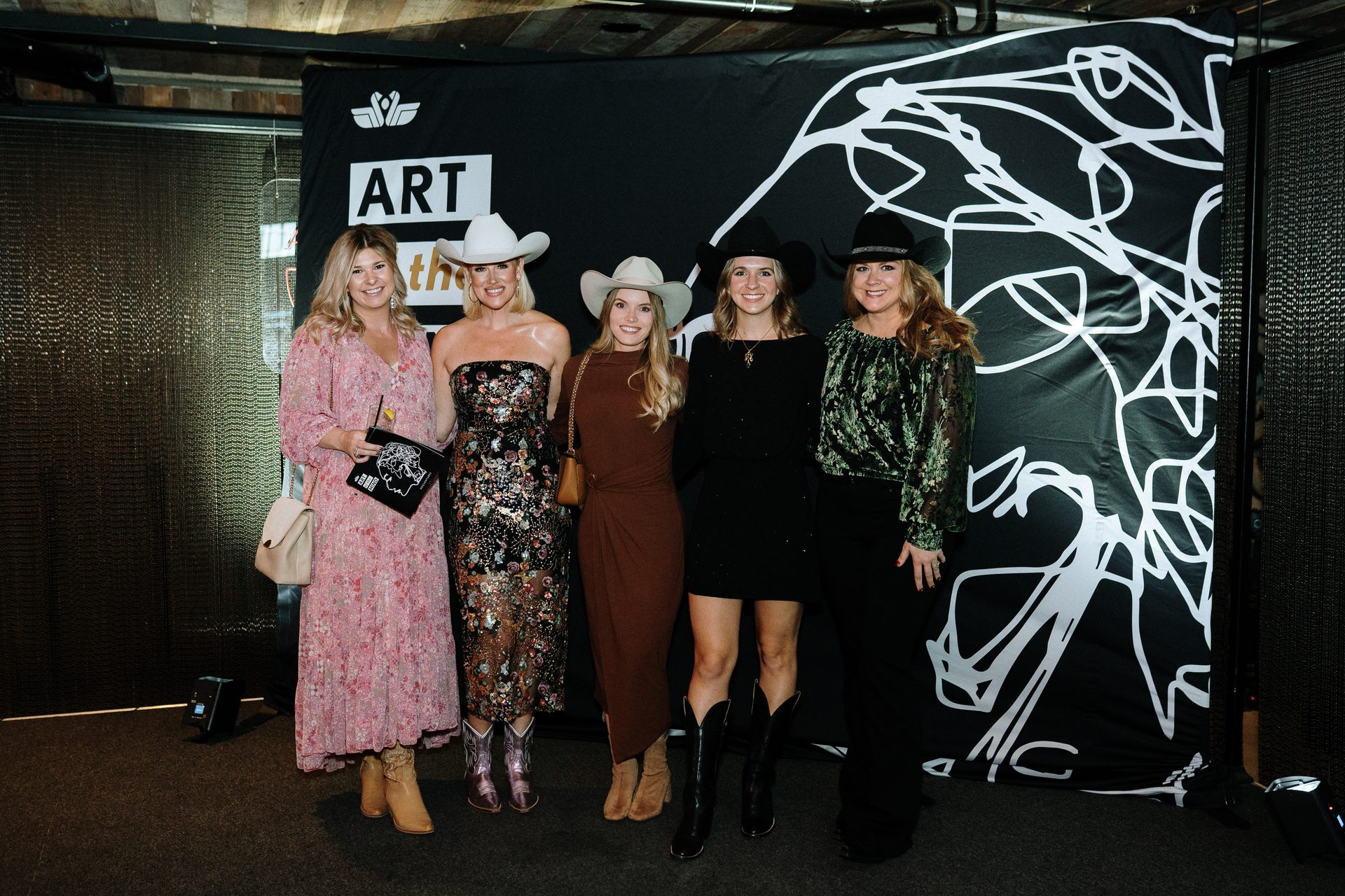 Five women in cowboy hats pose in front of an "ART" banner.