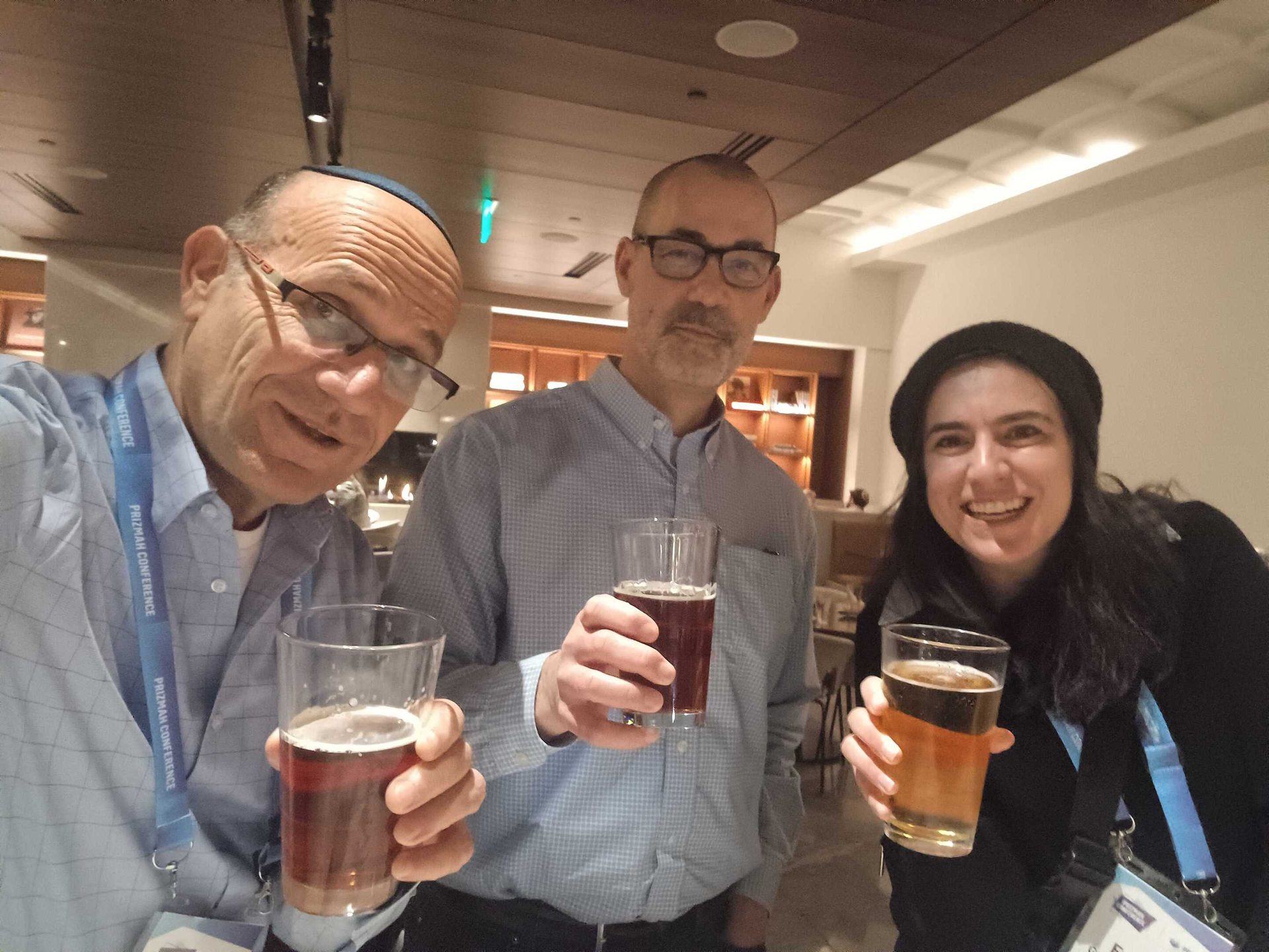 Three people smiling and holding beers at a conference.