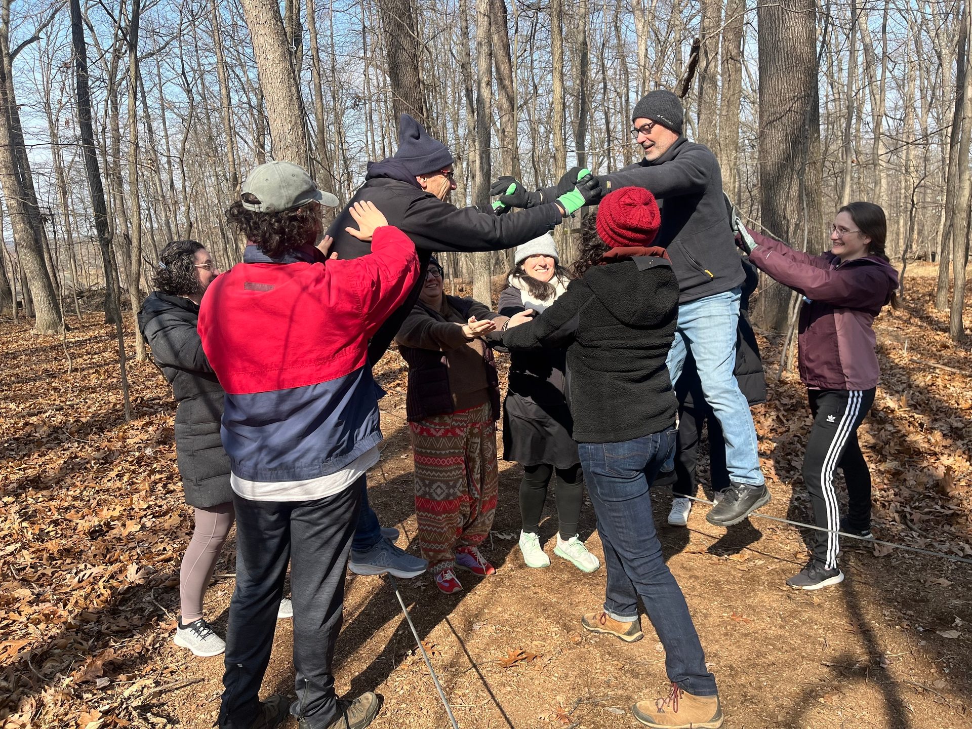 Team building in a forest: people support another person held elevated off the ground.