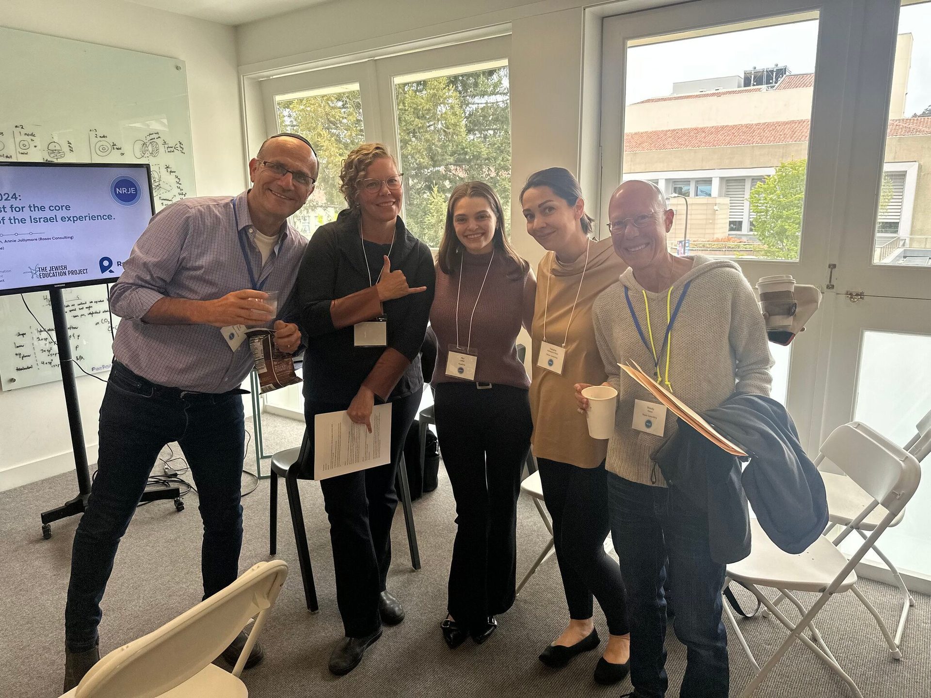 Five smiling people at a Jewish education event pose for a group photo indoors.