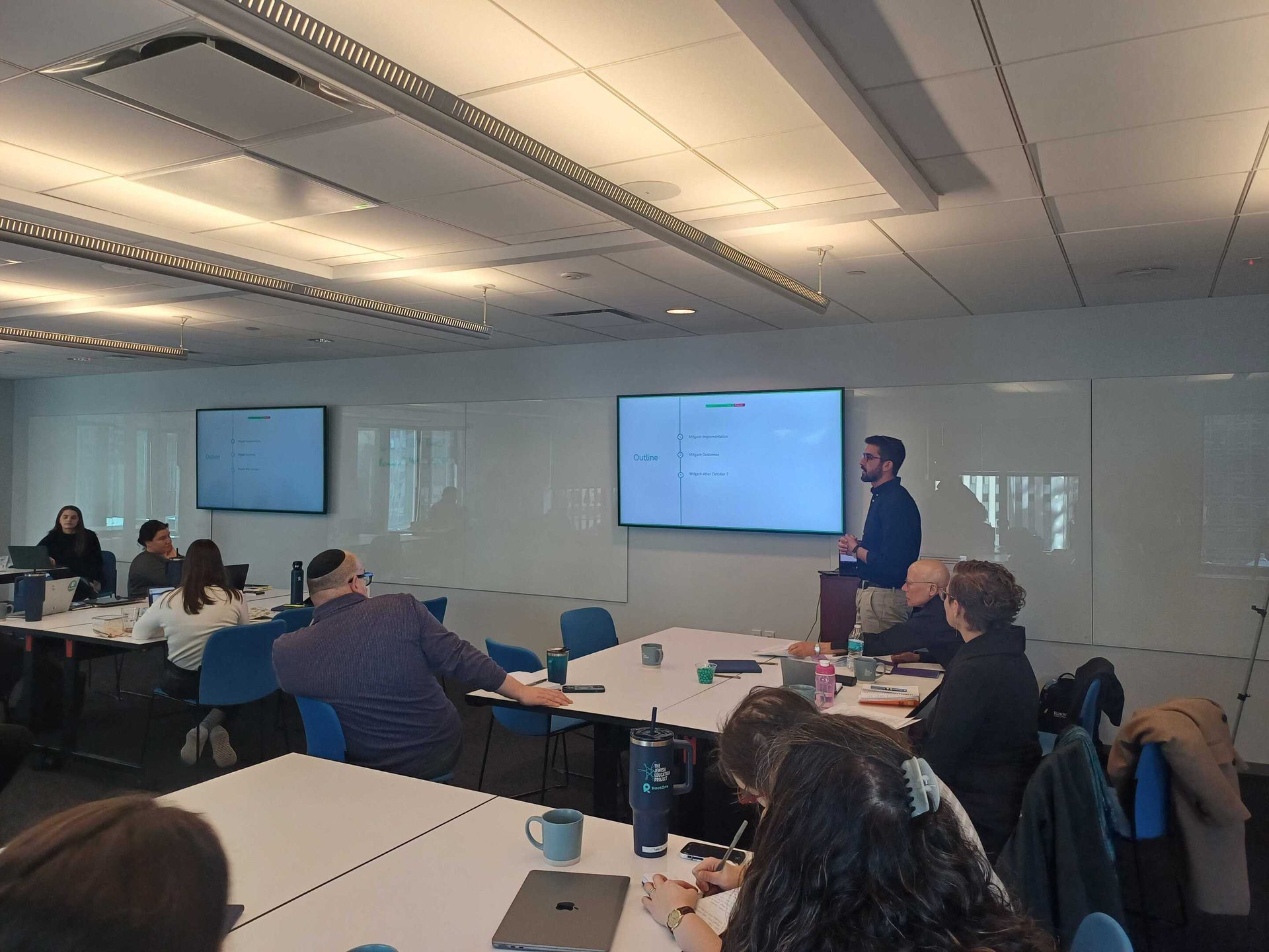A presenter addresses an audience in a bright conference room.