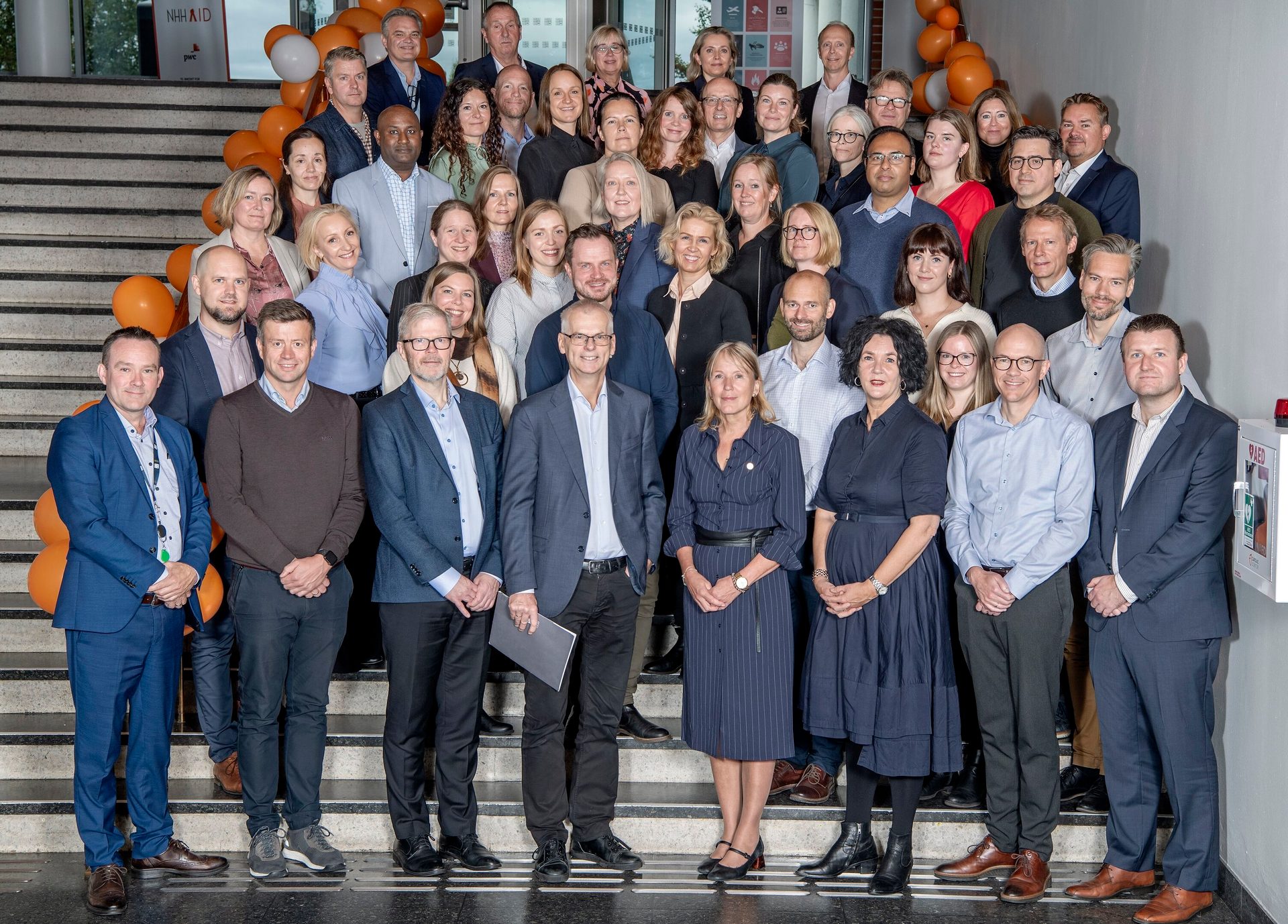 A large group of adults in business attire gathered on a staircase with orange balloons.