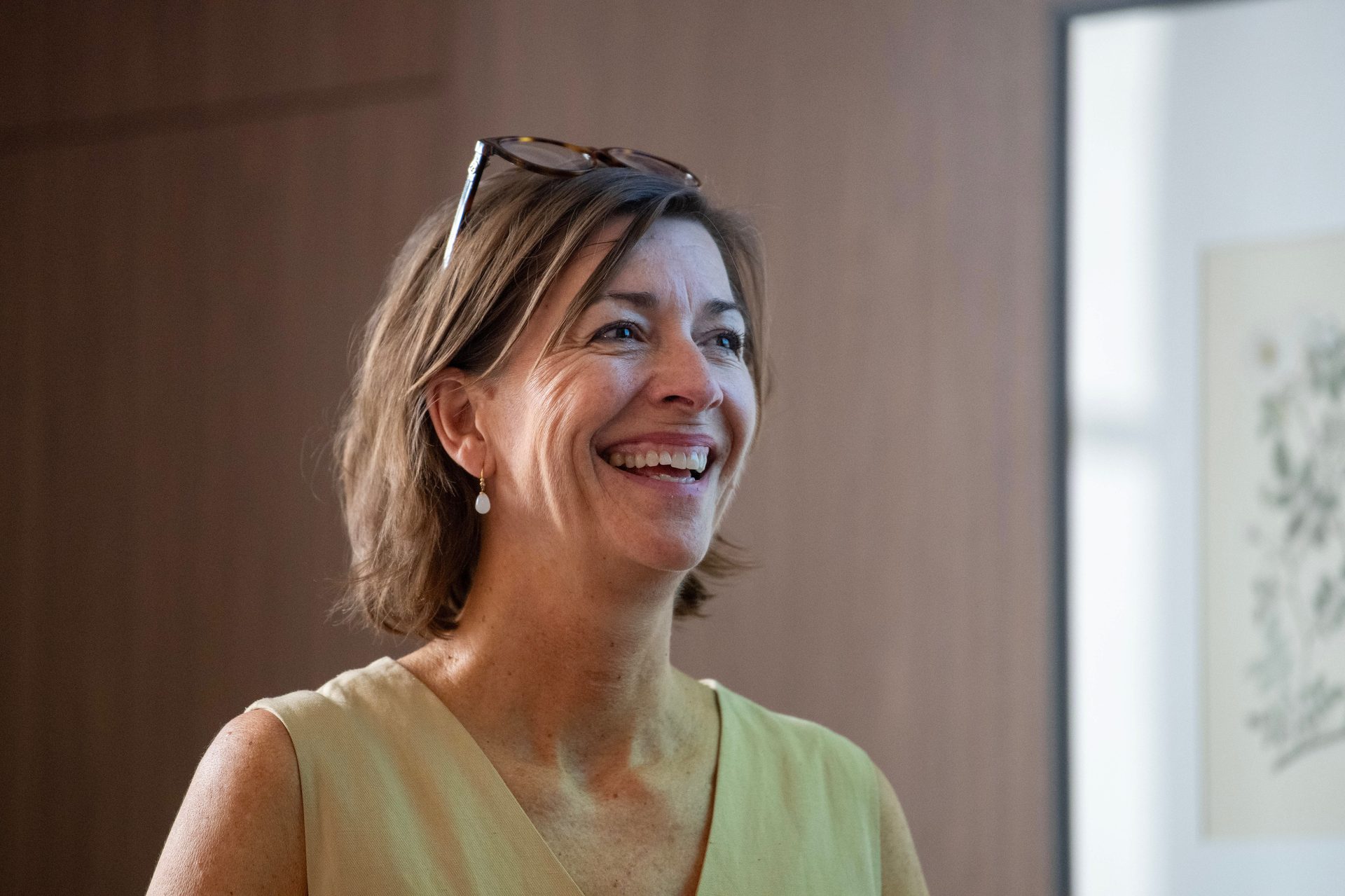 A smiling woman with glasses on her head, looking upwards and to the right.