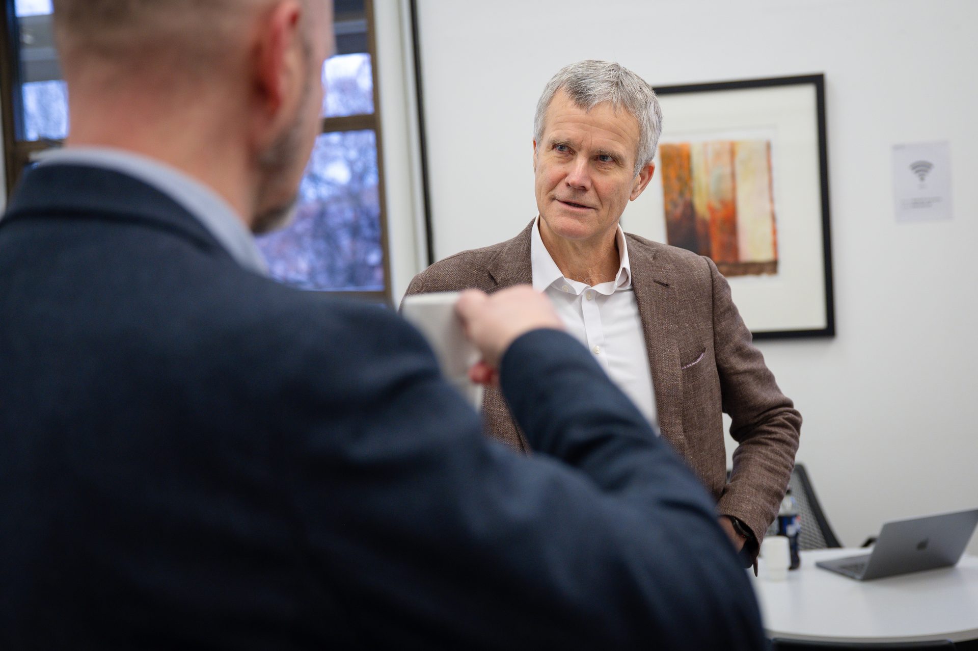 Two men conversing; one from behind holding a cup, the other listening intently.
