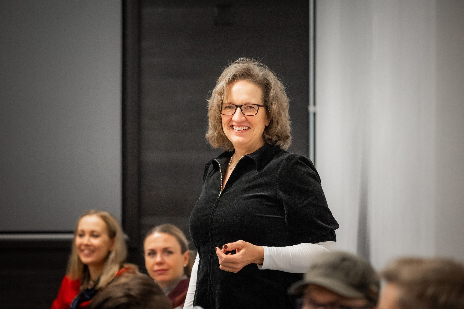 Smiling woman in glasses presenting to a group.