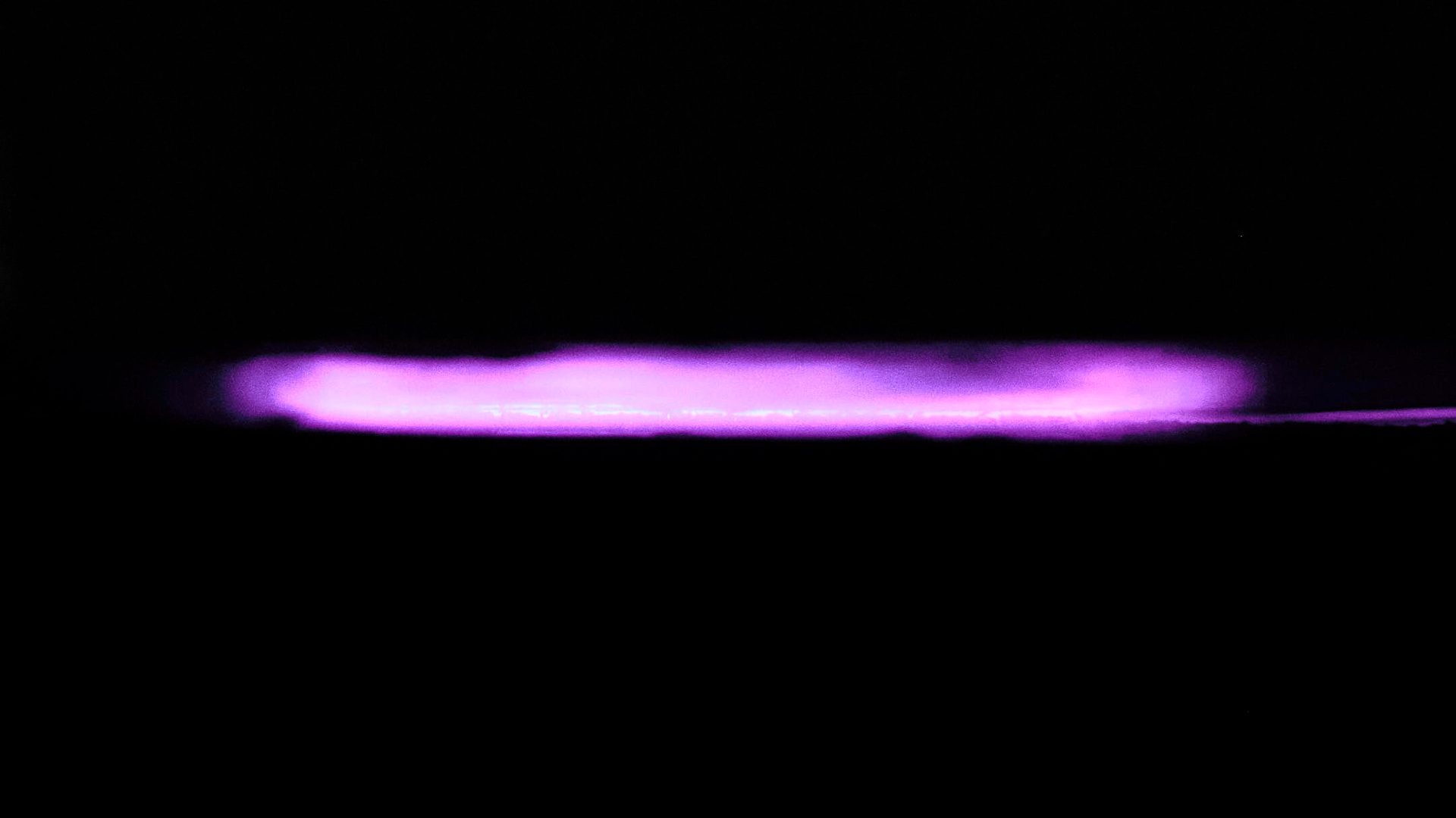 A vibrant, horizontal purple light beam glowing intensely against a dark background, resembling plasma or neon.