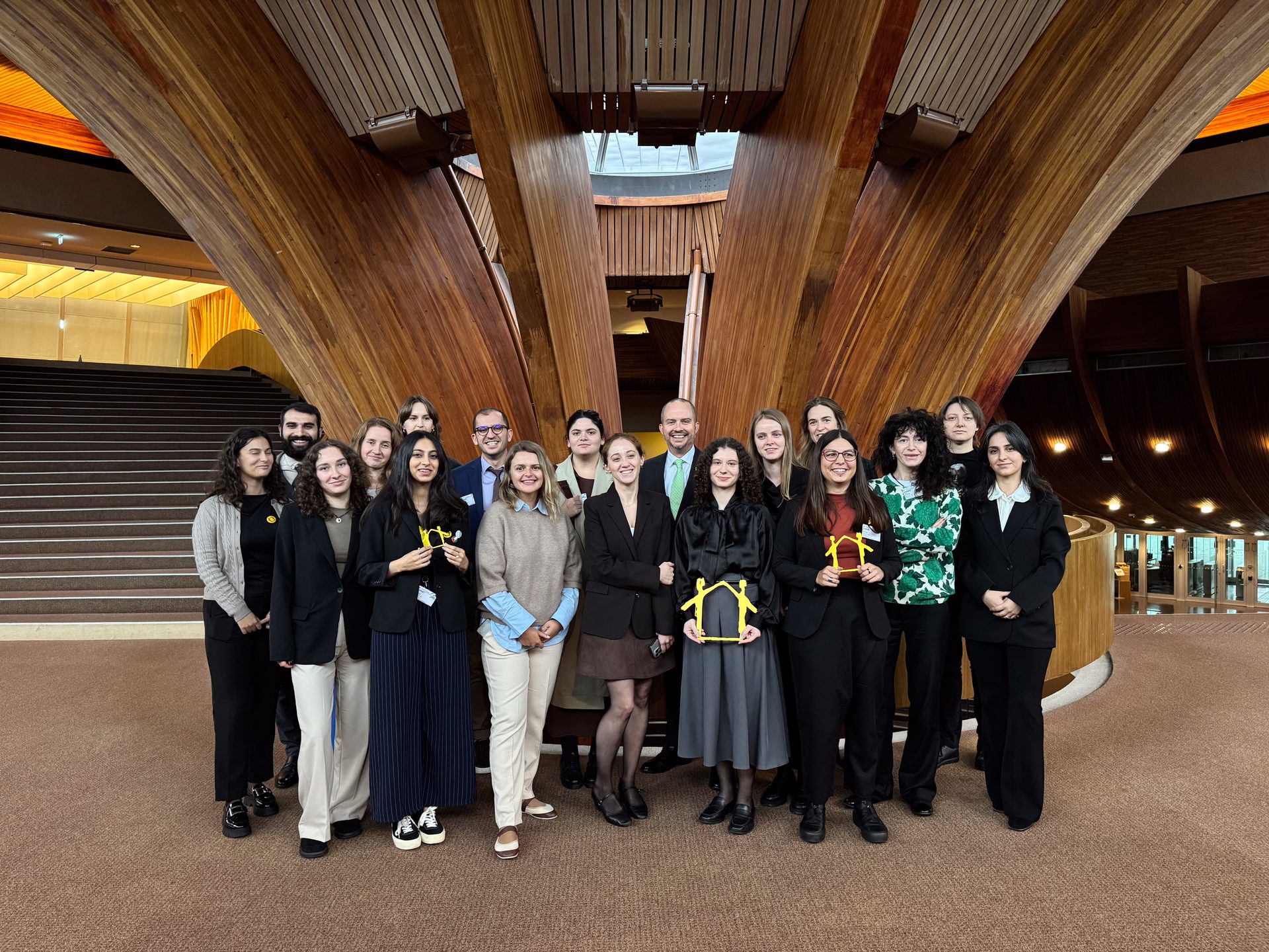 Group of young adults posing with house-shaped awards in a building with wooden architecture.