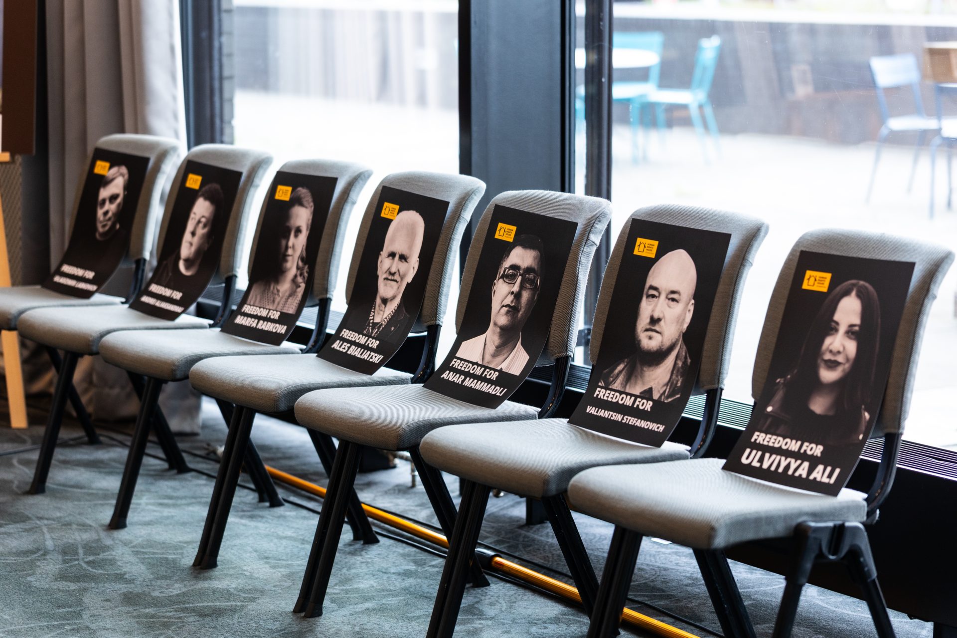 A row of chairs, each displaying a portrait and 'FREEDOM FOR [NAME]' sign, advocating for human rights.