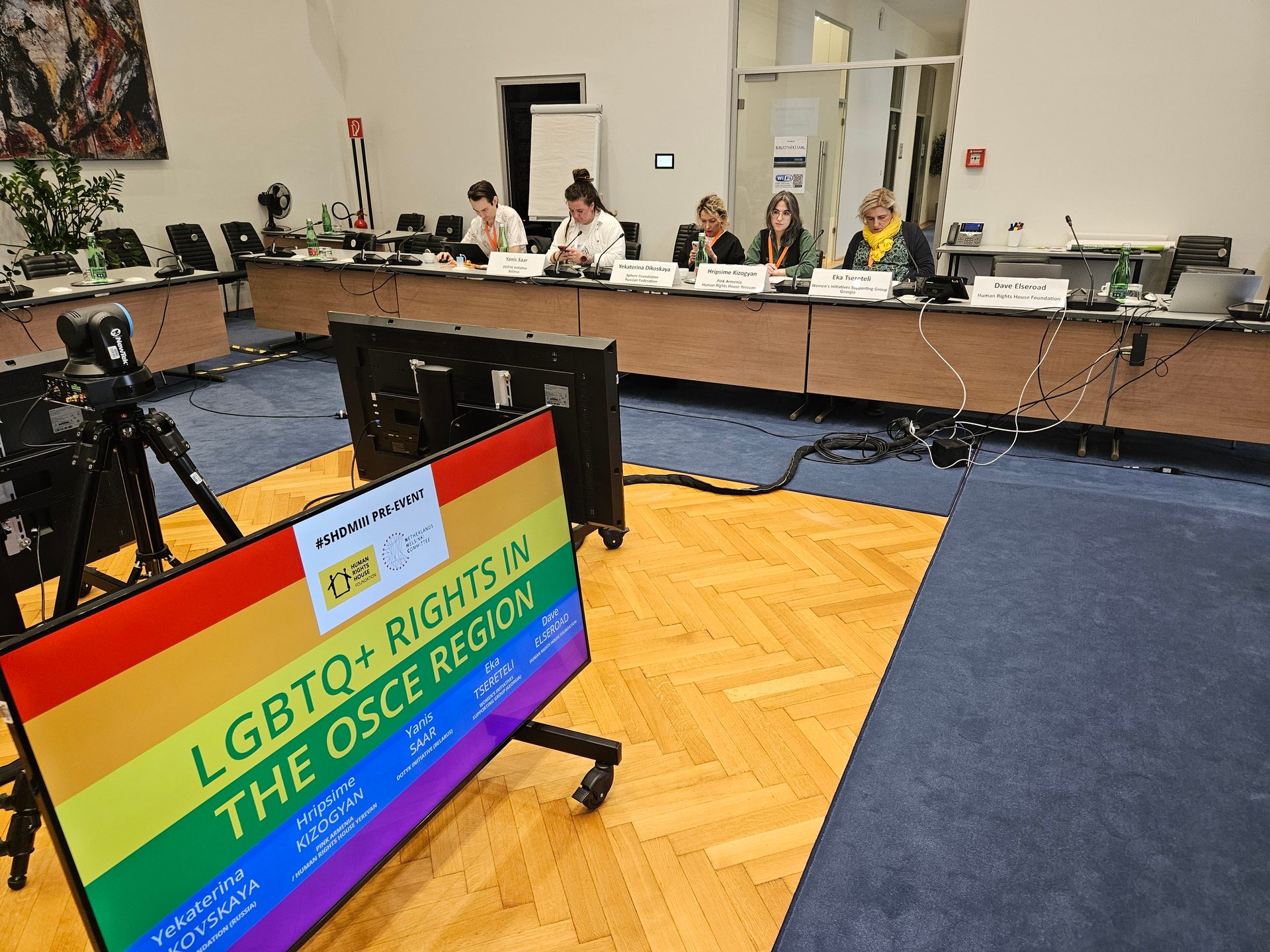 Five panelists at a table with an event screen in the foreground displaying 'LGBTQ+ RIGHTS IN THE OSCE REGION'.