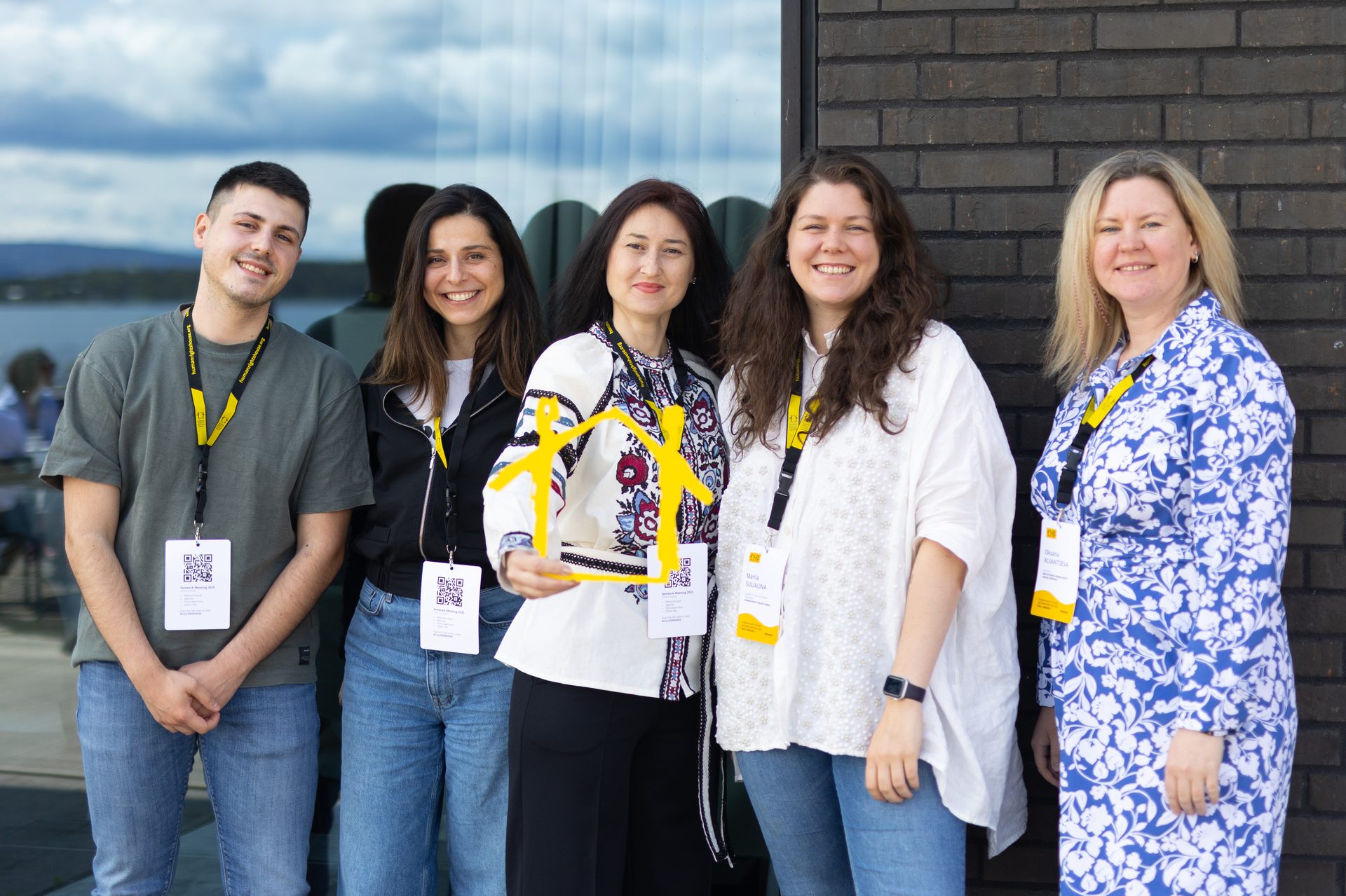 Five smiling people, some holding a yellow house-shaped award, at an outdoor event.