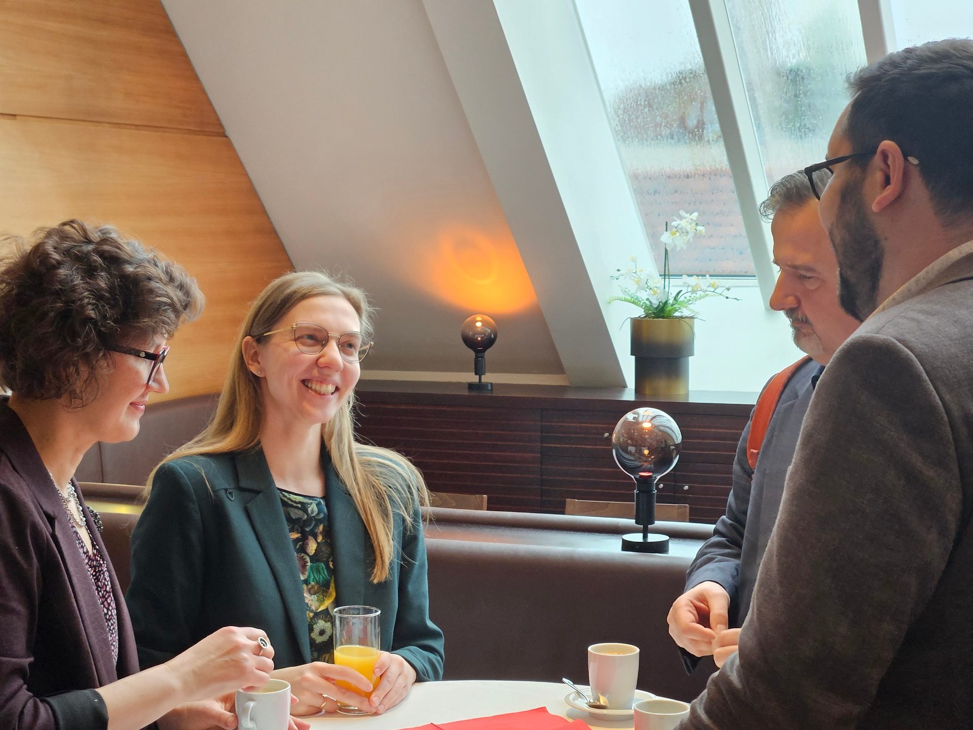 Four people gathered around a table with drinks, engaged in a lively conversation inside a cafe.