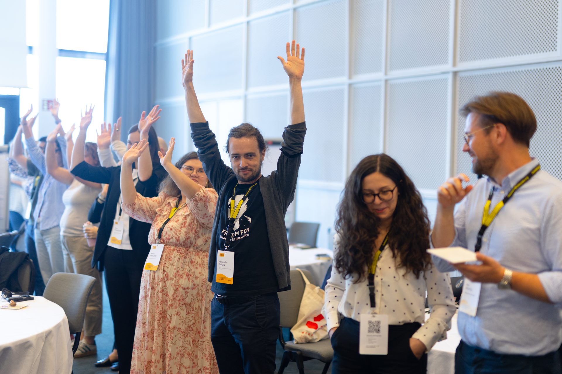 Attendees at an event or conference, some with hands raised, others observing.