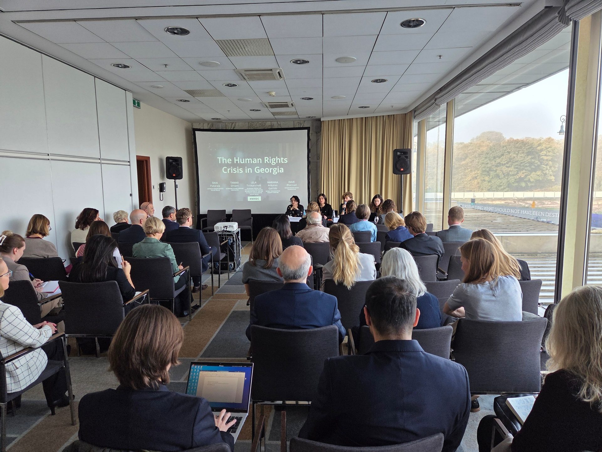 People attending a conference on "The Human Rights Crisis in Georgia" with a panel and screen.