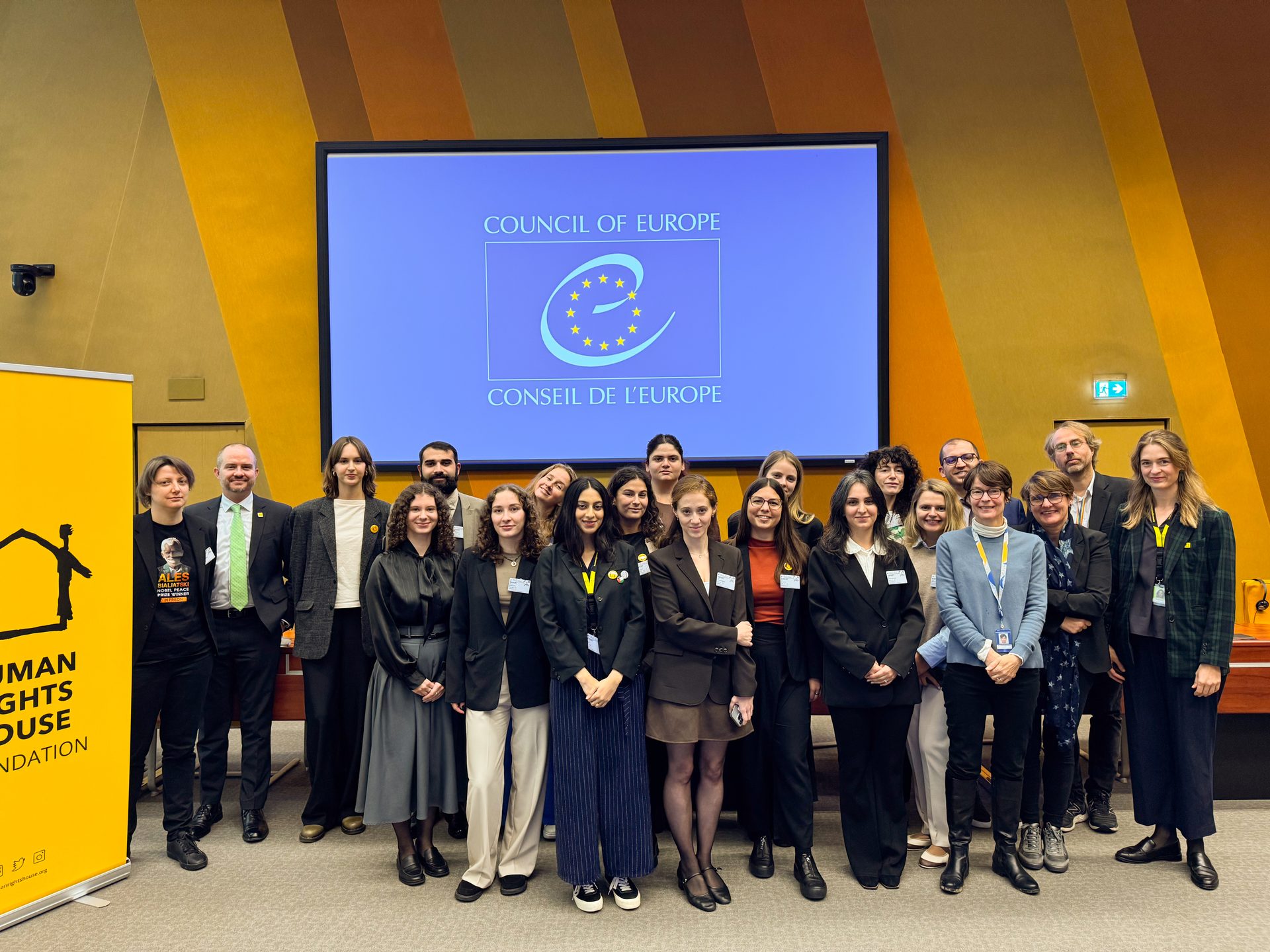 A diverse group of people, including youth and adults, stands before a "Council of Europe" screen and a human rights banner.