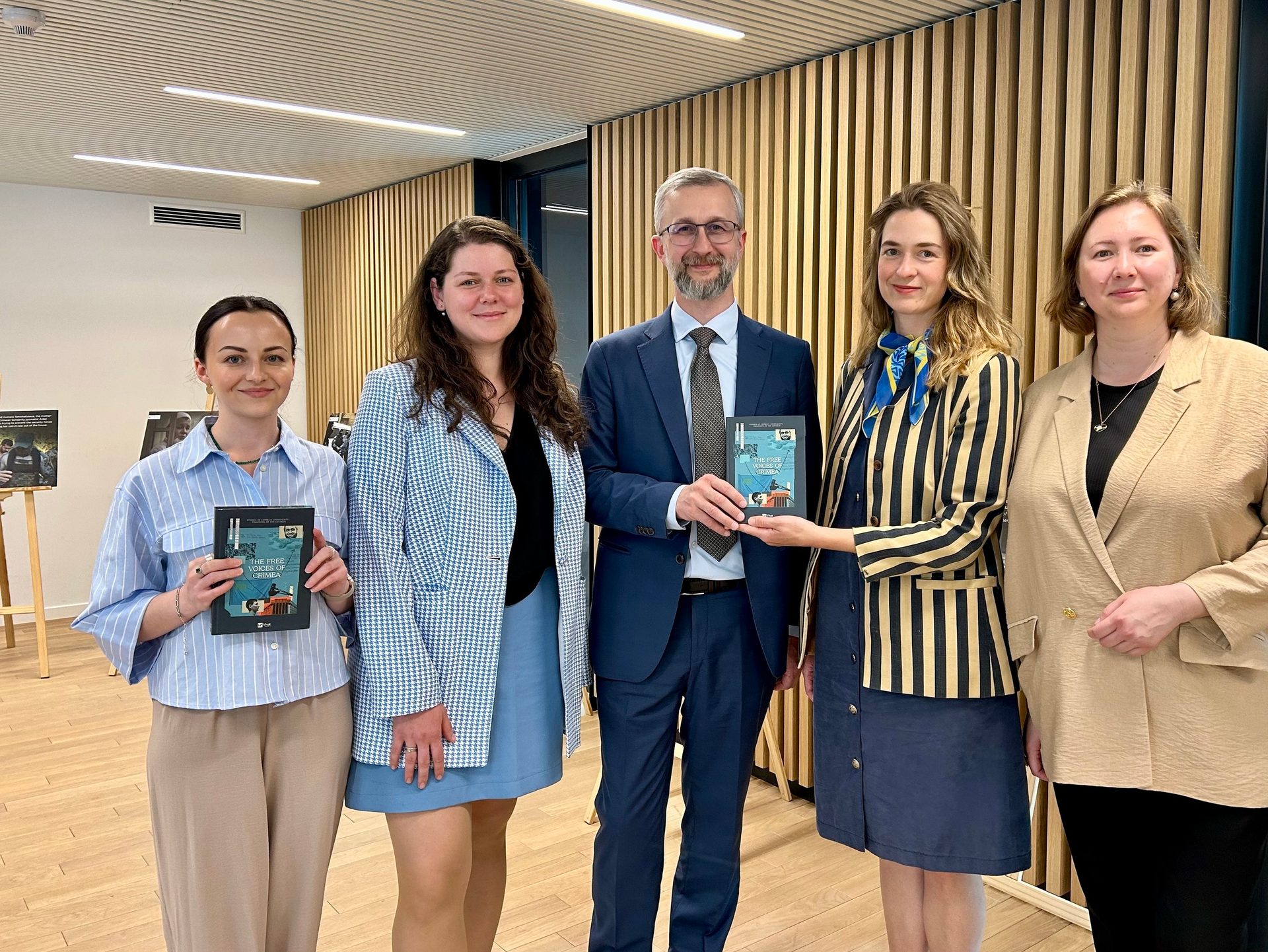 Five people, three women and two men, holding "THE FREE CRIMEA" books at an indoor event.