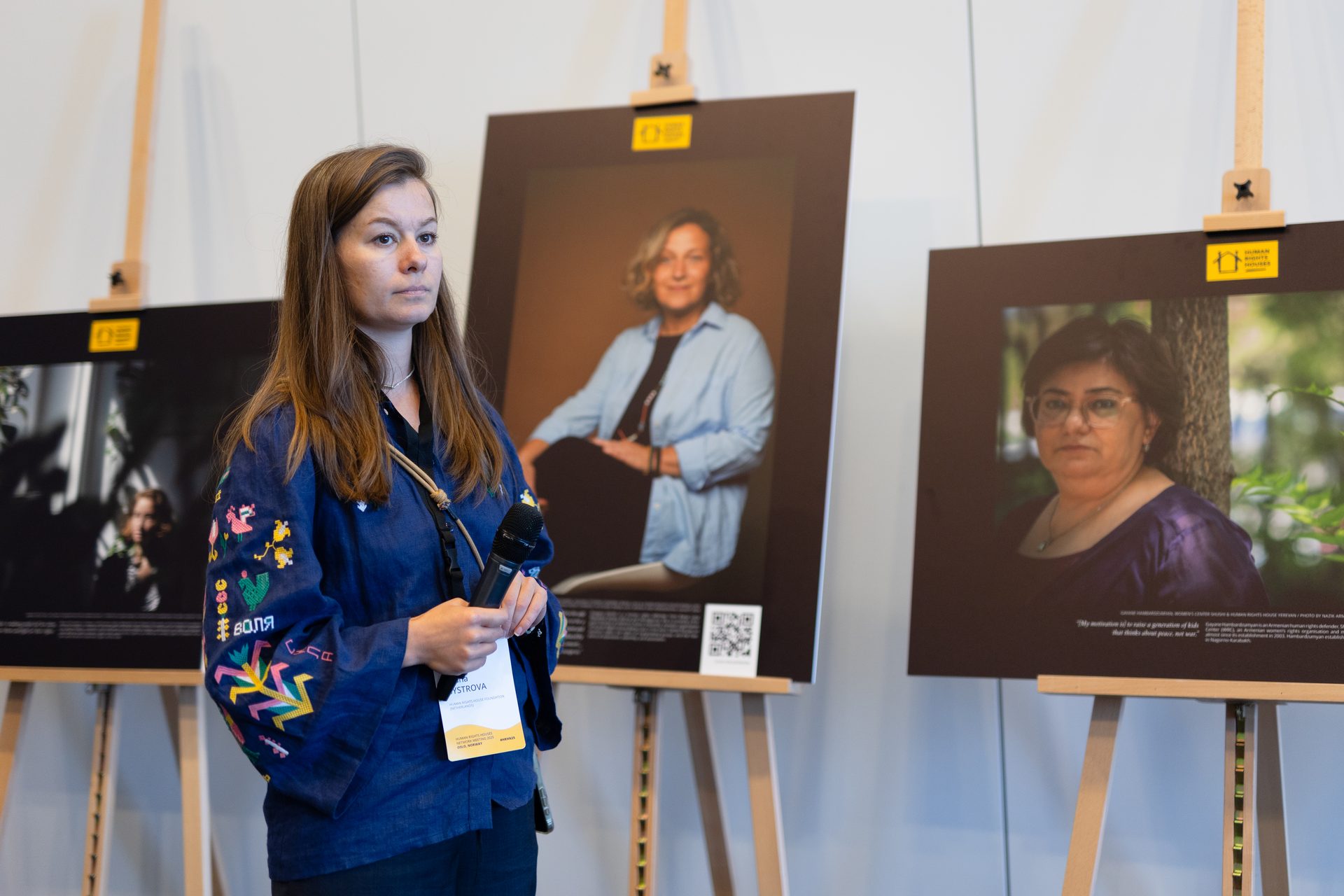 A woman presenting at an exhibition with portraits of other women on display.