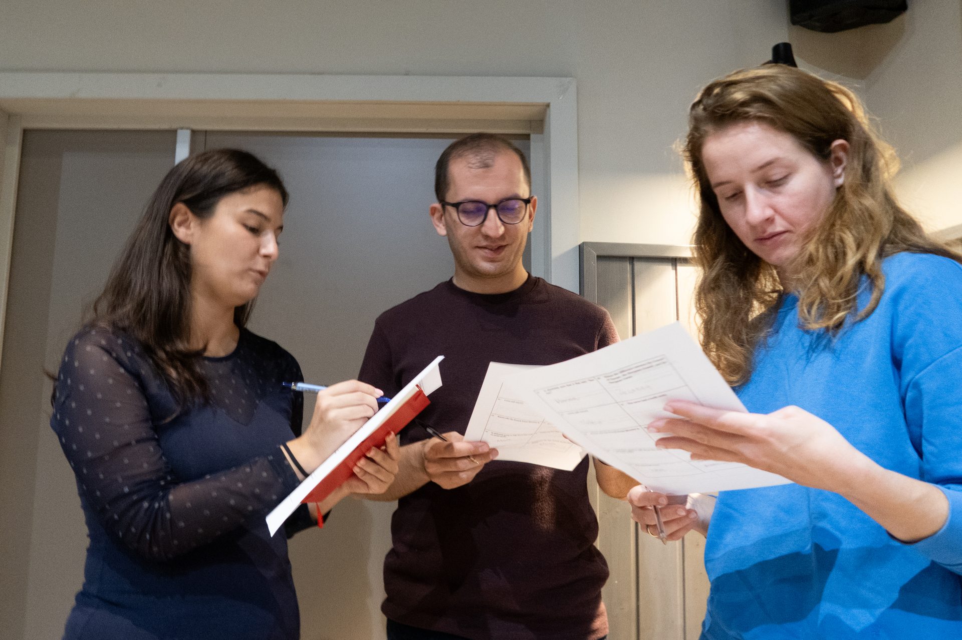 Three colleagues, two women and one man, standing and reviewing documents and notes together.
