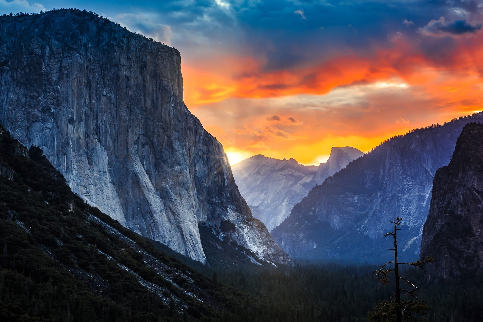 Yosemite Valley sunset, dramatic sky over towering cliffs and dark forest.