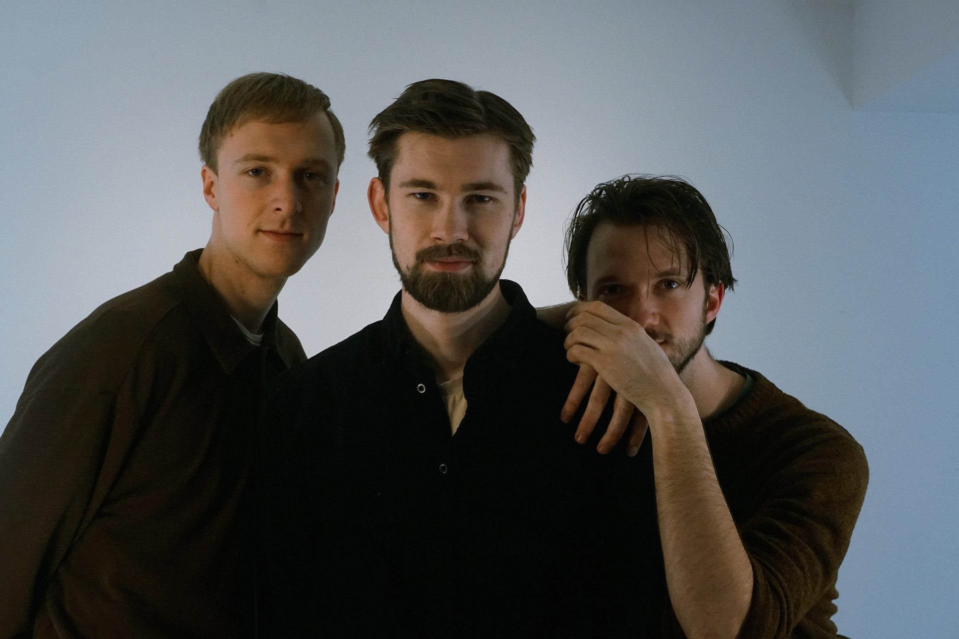 Three men posing for a portrait, one partially covering his face.