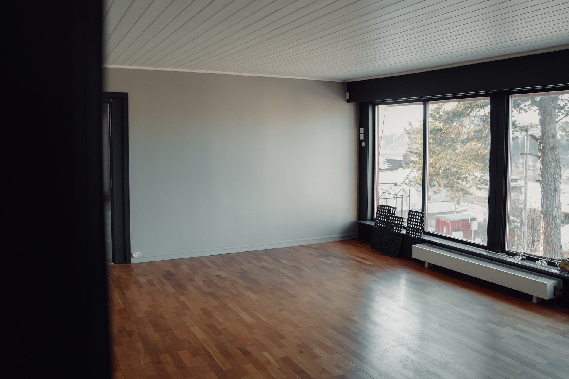 Empty room featuring a wooden floor, light grey walls, and large windows overlooking a winter landscape.