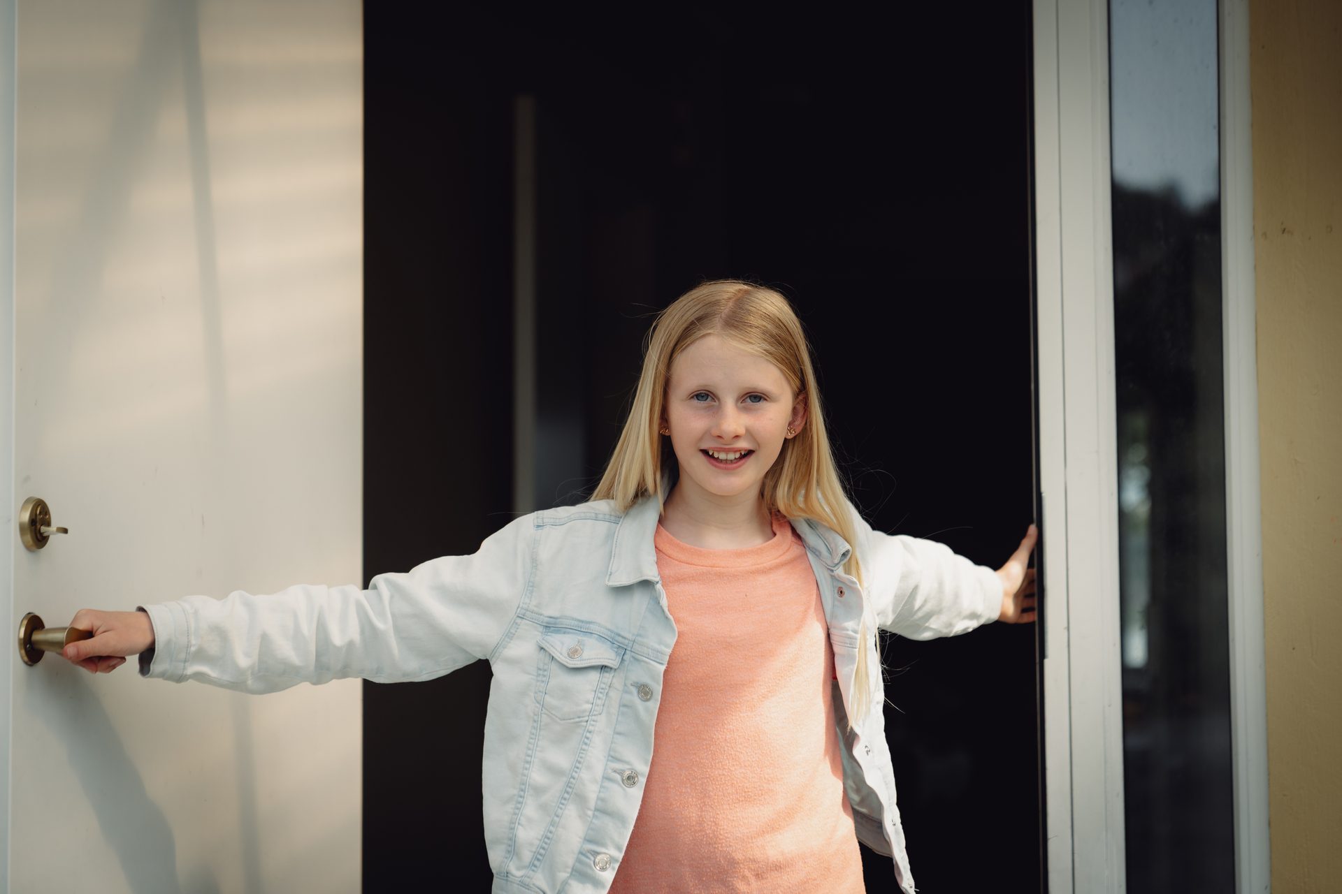 Smiling blonde girl in a denim jacket opens two doors, one white, one black.
