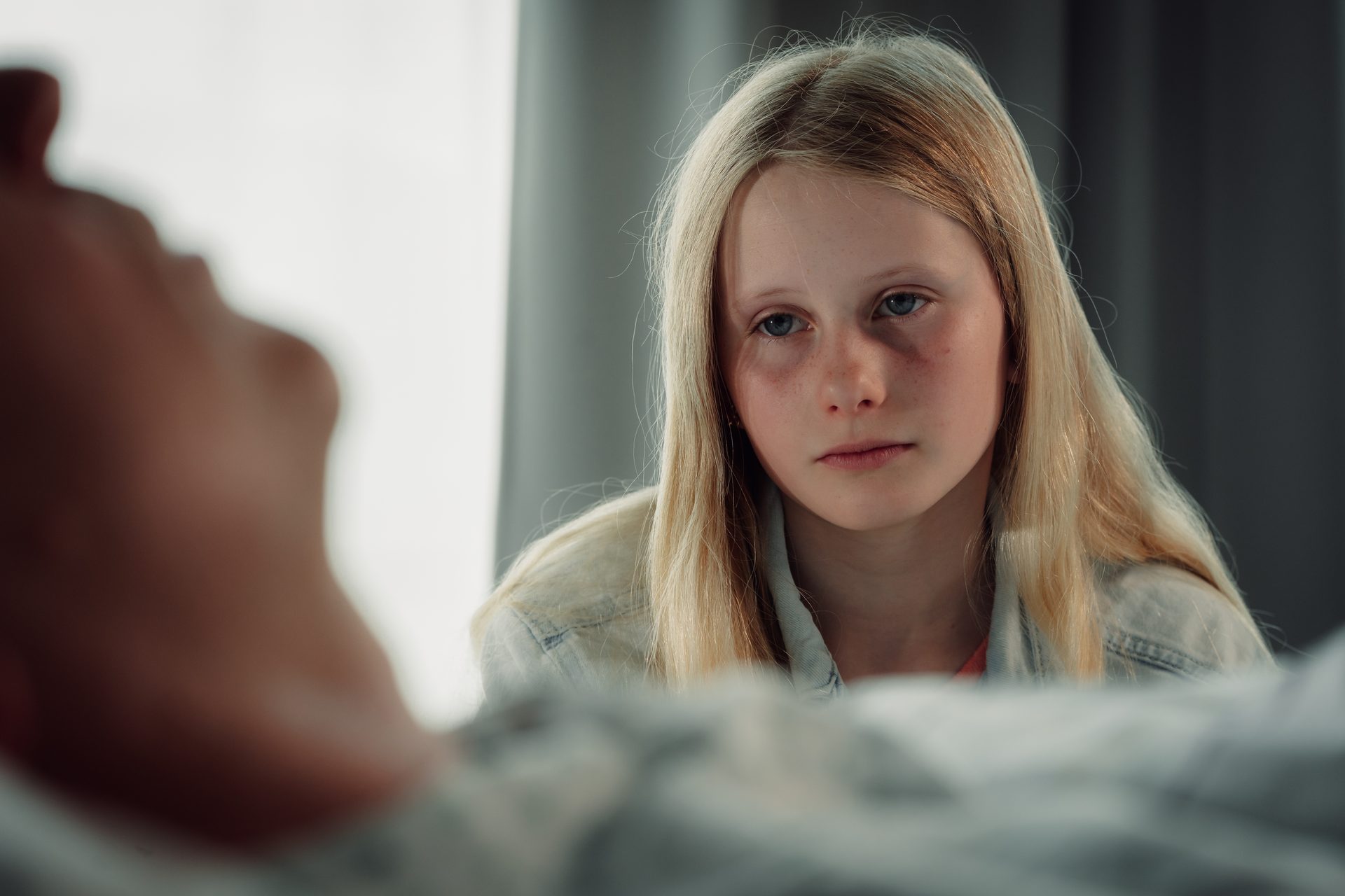 Blonde girl with red eyes looks sadly at a blurry figure in the foreground.