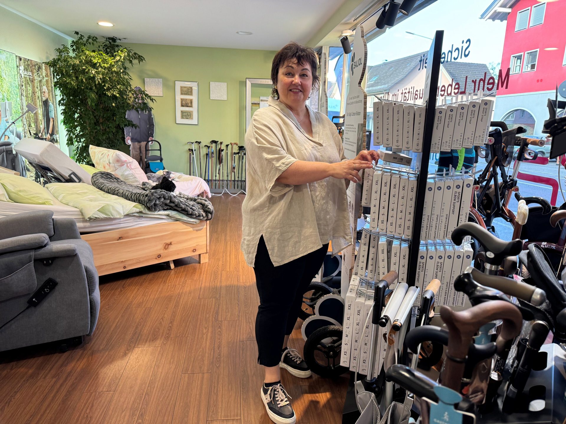 A smiling woman stands next to a display of medical supports and equipment in a store, with a hospital bed in the background.
