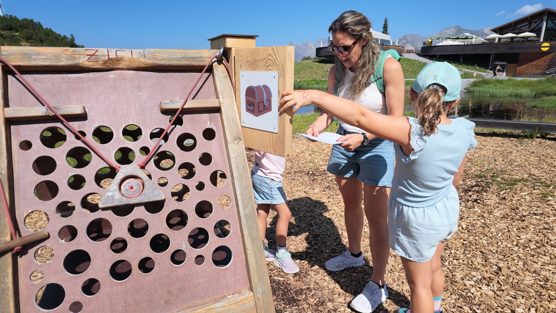 Woman and children engaged in a treasure hunt game on a unique wooden play structure with holes in the mountains.
