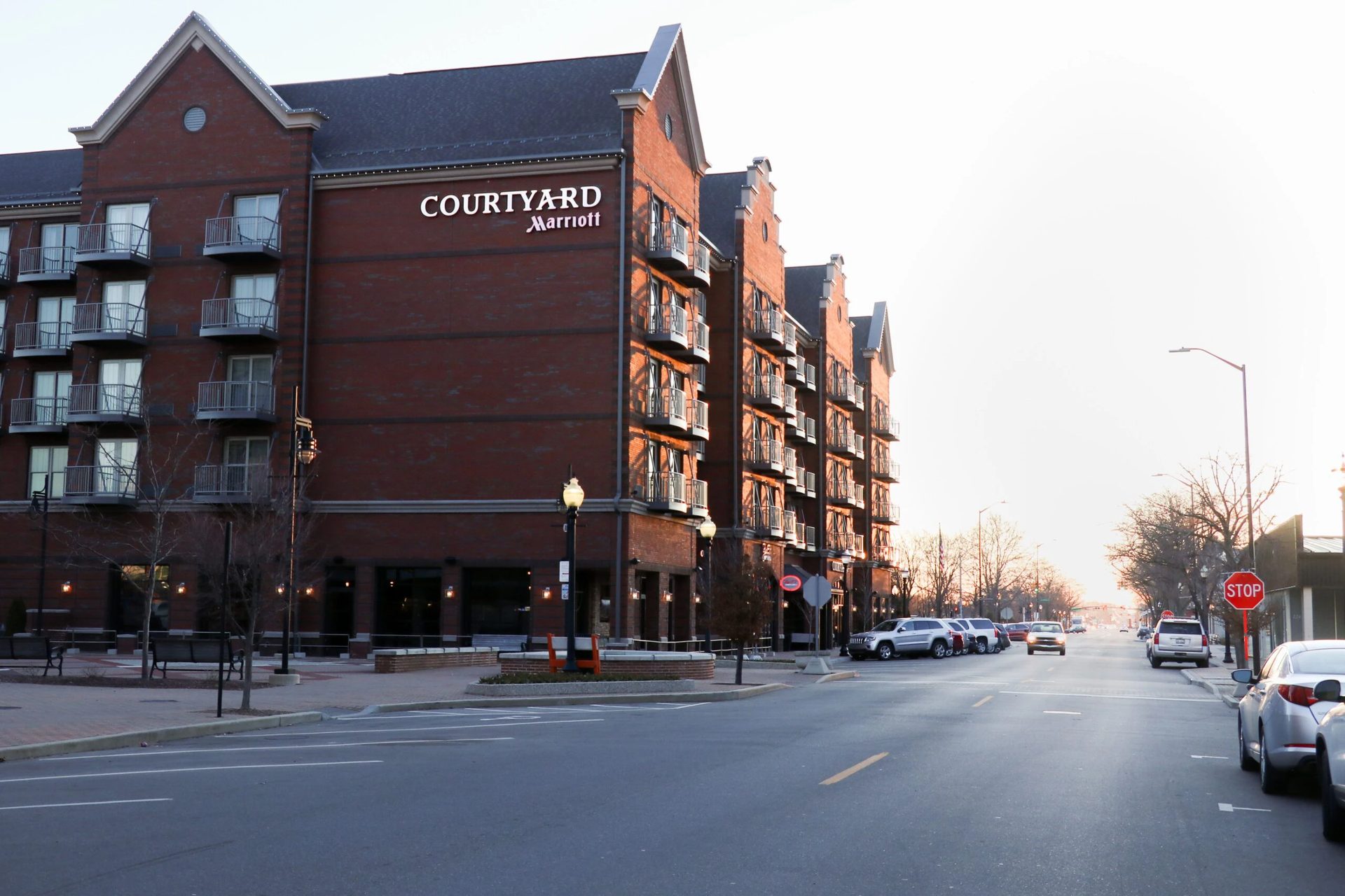 A brick Courtyard Marriott hotel building with balconies next to a street with cars and a stop sign.