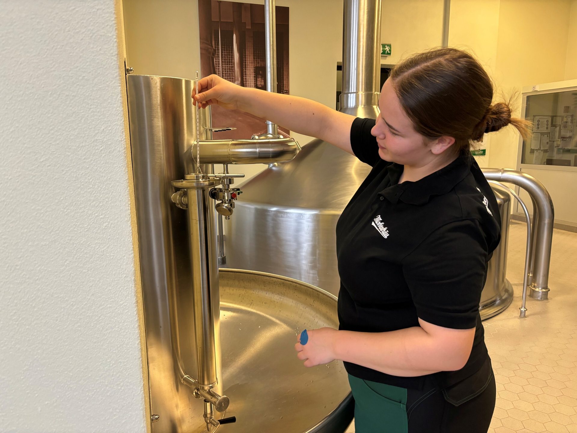 A woman measures liquid in a large brewery tank with a thermometer.