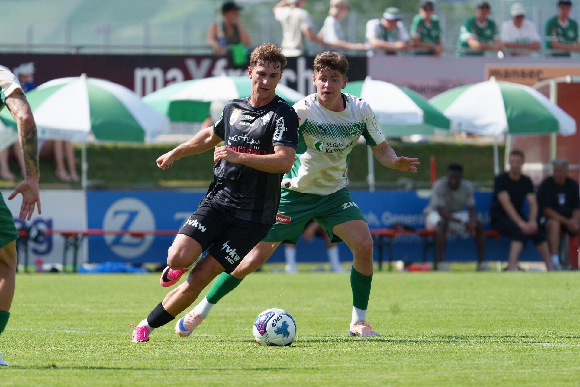 Two soccer players, one in black and one in white, compete for the ball on a green field.