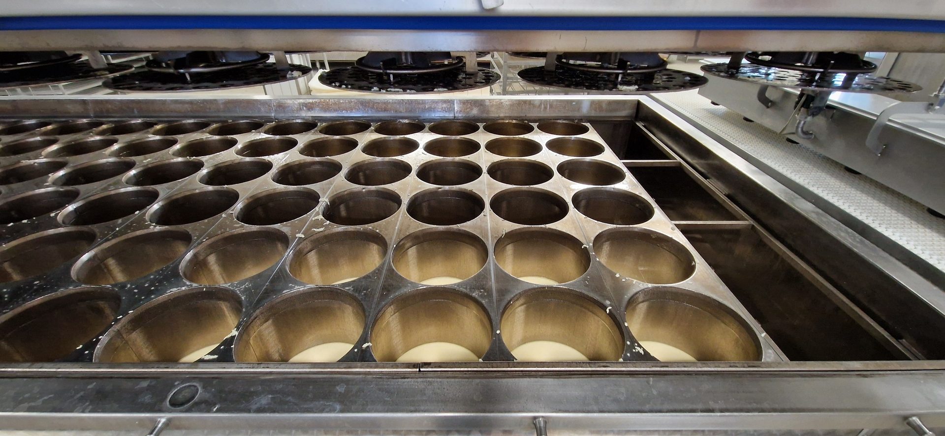 Automated machine with a grid of circular molds filled with white batter on a production line.