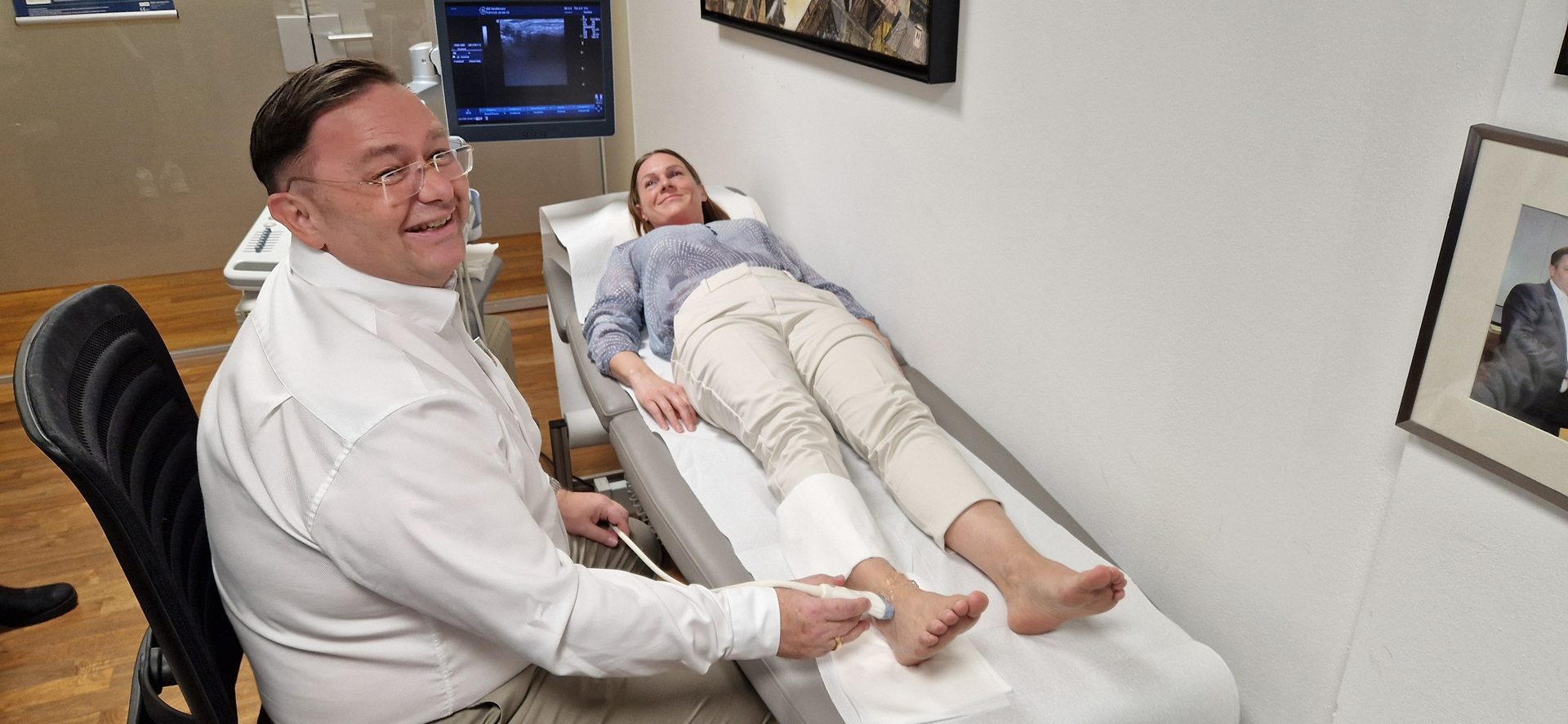 Smiling male doctor performs an ultrasound on a female patient's foot.