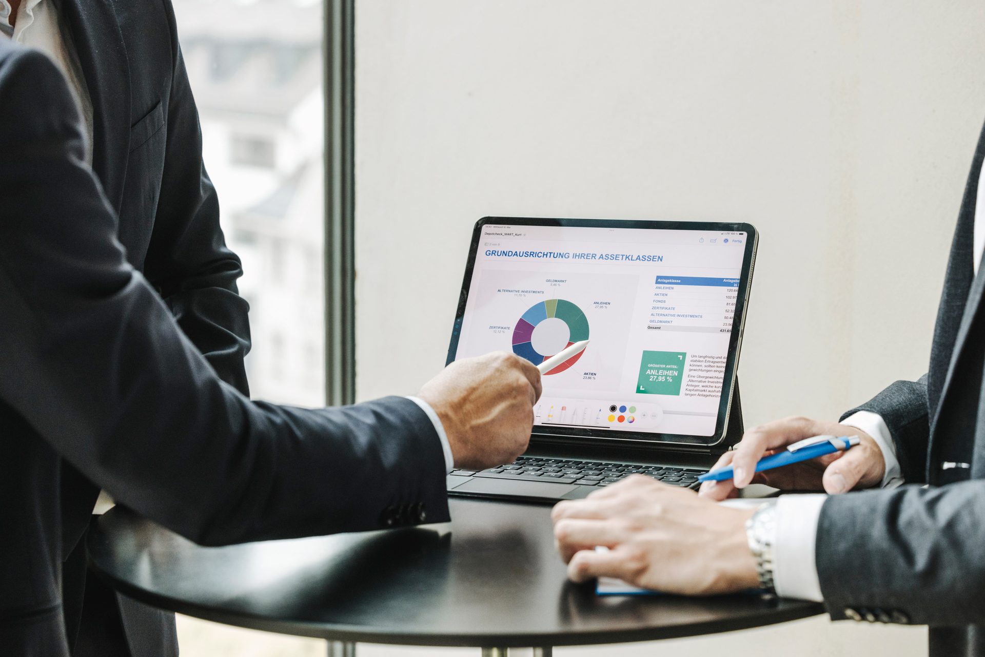 Businesspeople analyze investment data on a tablet with a pie chart.
