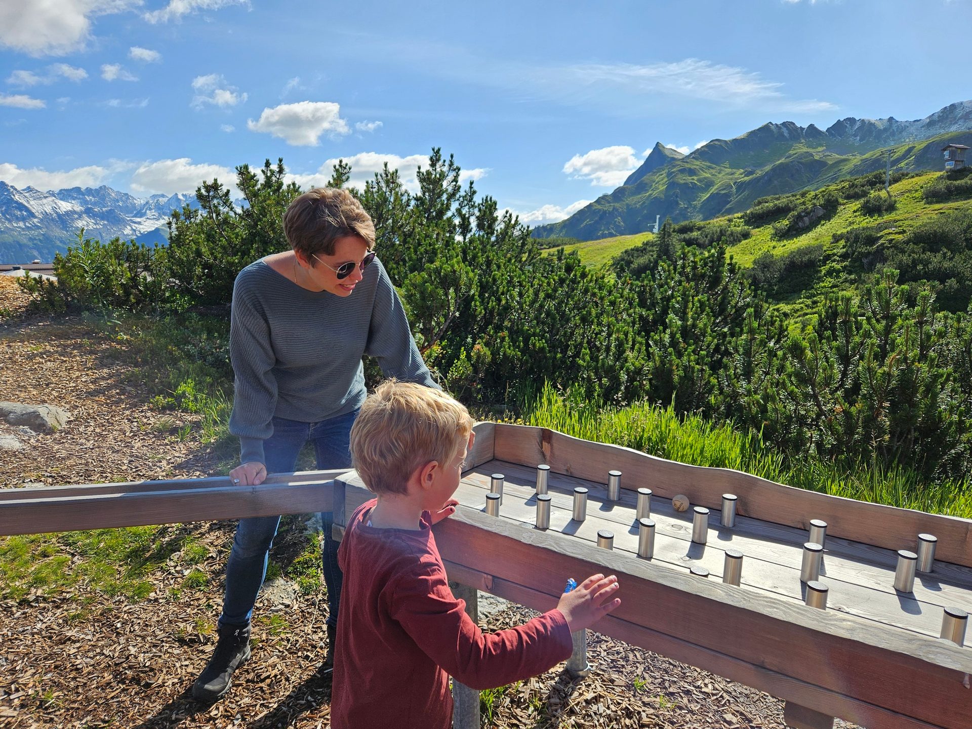 Woman and child playing a wooden ball game outdoors, with mountains in the sunny background.