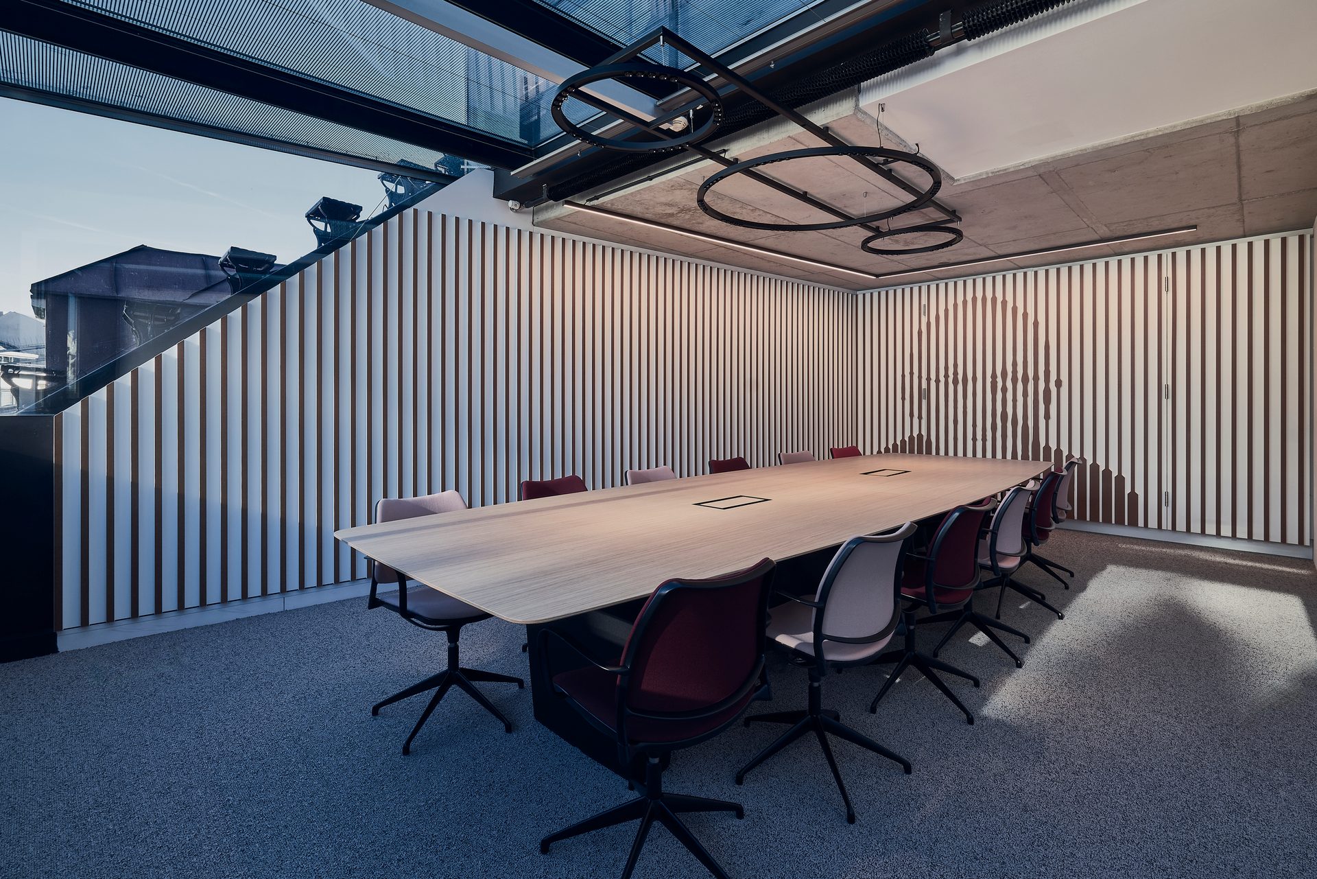 Modern conference room with a long table, ergonomic chairs, city skyline wall art, and unique circular ceiling light.