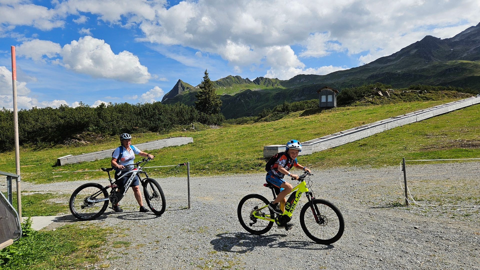 Woman and boy with helmets on e-bikes on a gravel path in a mountainous landscape.
