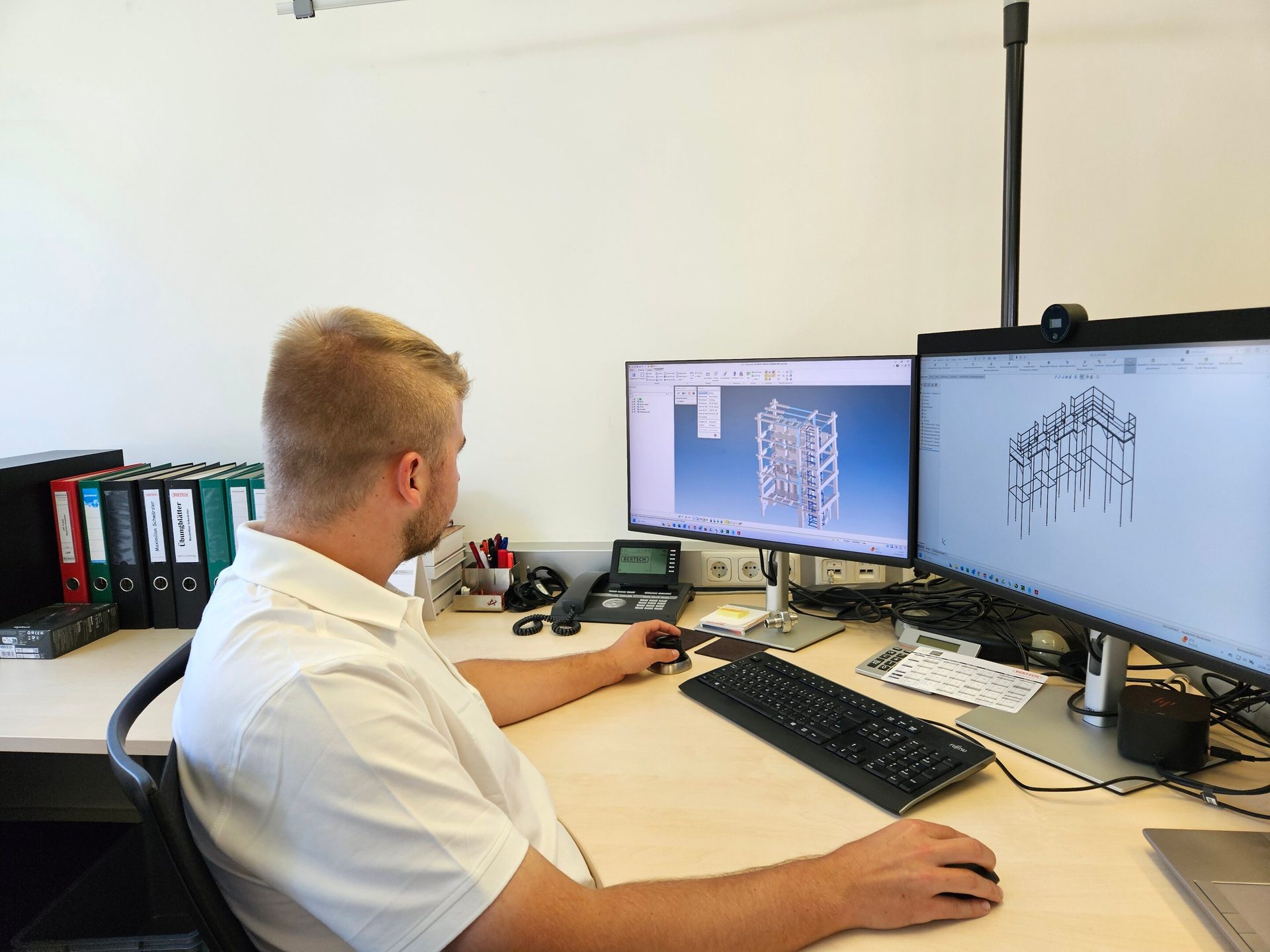 Man at a desk, using CAD software on dual monitors to view 3D engineering models.